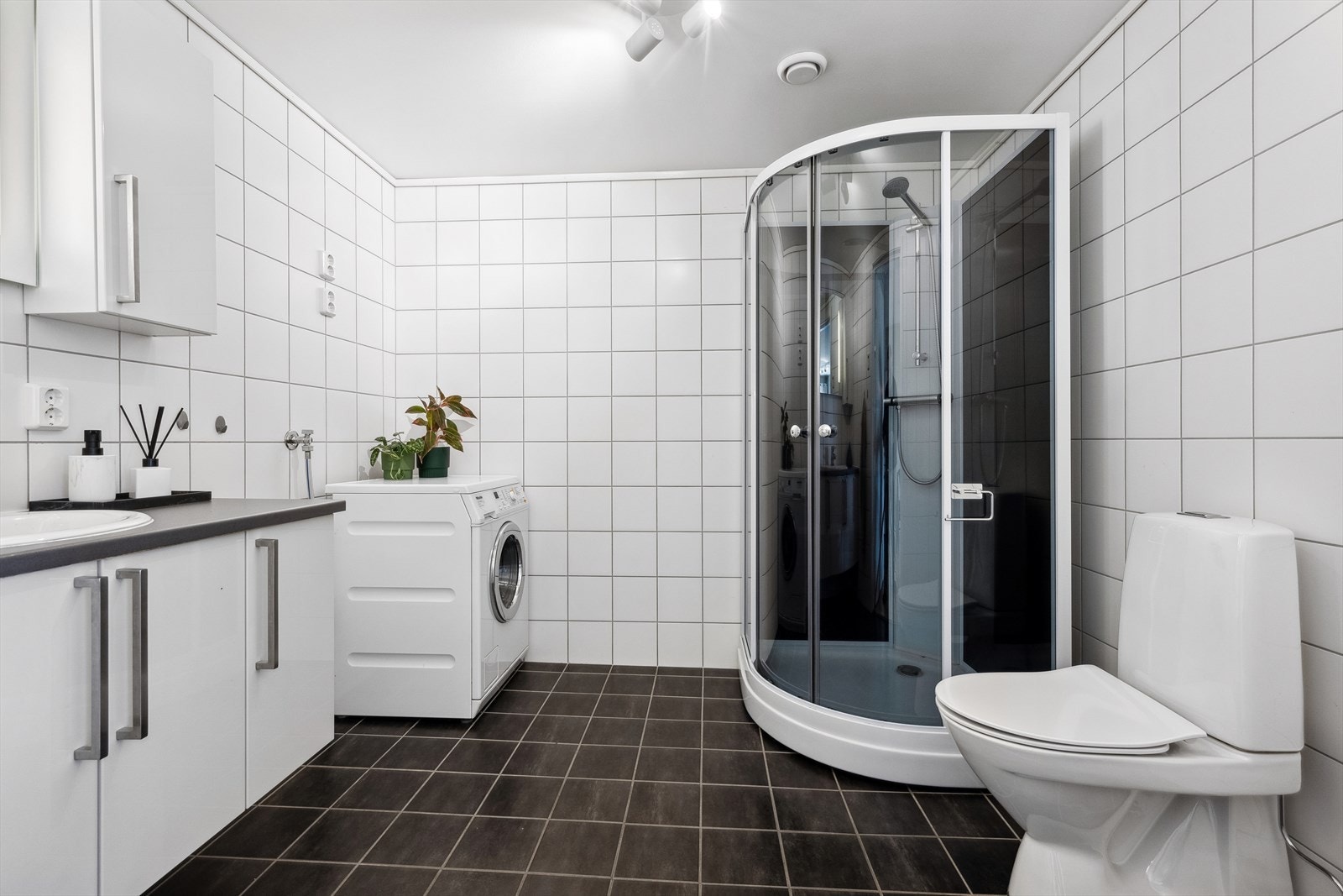 Badet inneholder baderomsinnredning med servant, dusjnisje med glassdører, gulvmontert wc og det er opplegg for vaskemaskin. Galleribilde
