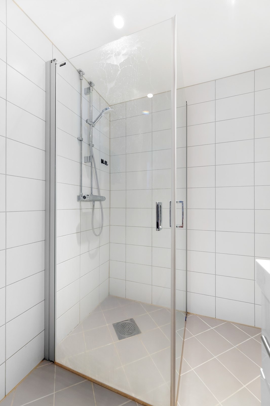 Videre er badet utstyrt med dusjhjørne med innfellbare glassvegger, servantinnredning med skuffer og overskap, samt opplegg og plass til vaskemaskin Galleribilde