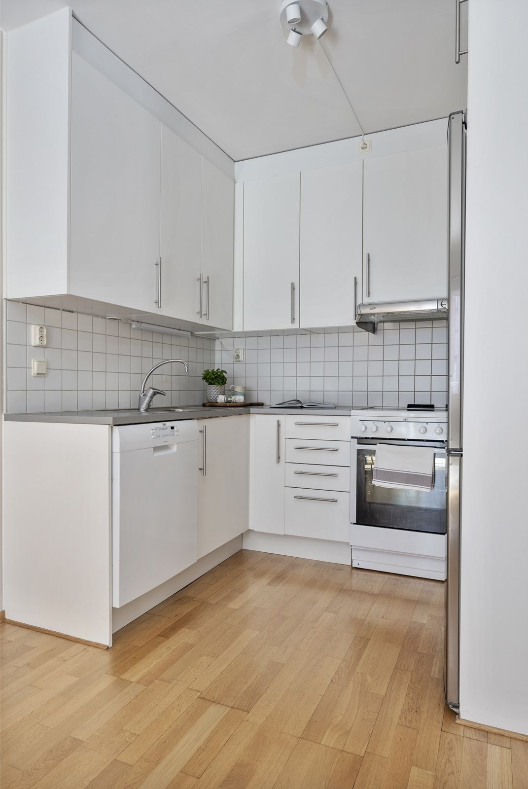 Pent kjøkken innredet med hvite, slette fronter og benkeplate i laminat Galleribilde