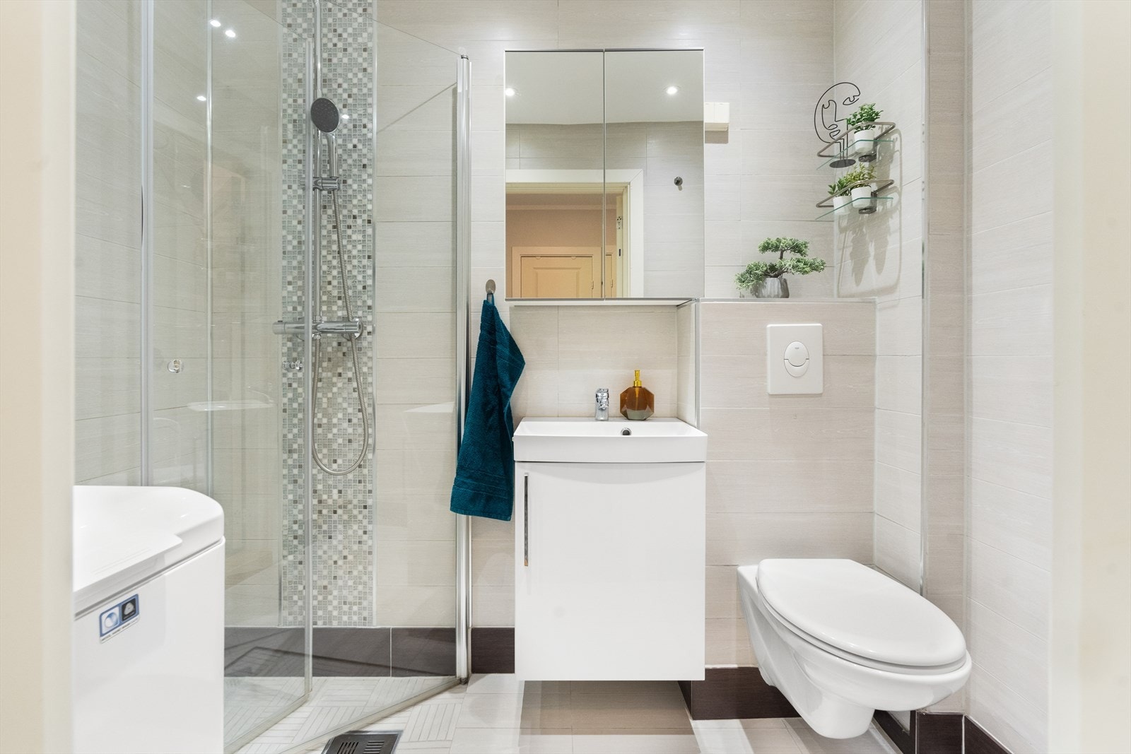 Badet inneholder speilinnredning, downlights, vegghengt toalett og dusj i hjørne bak svingbare glassdører Galleribilde