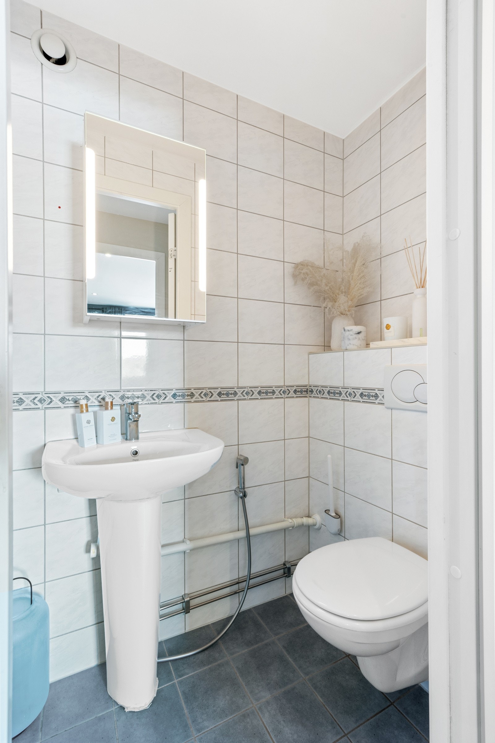 Lyst og pent flisvalg, vegghengt wc, pyntekant og servant med speilskap på vegg. Galleribilde