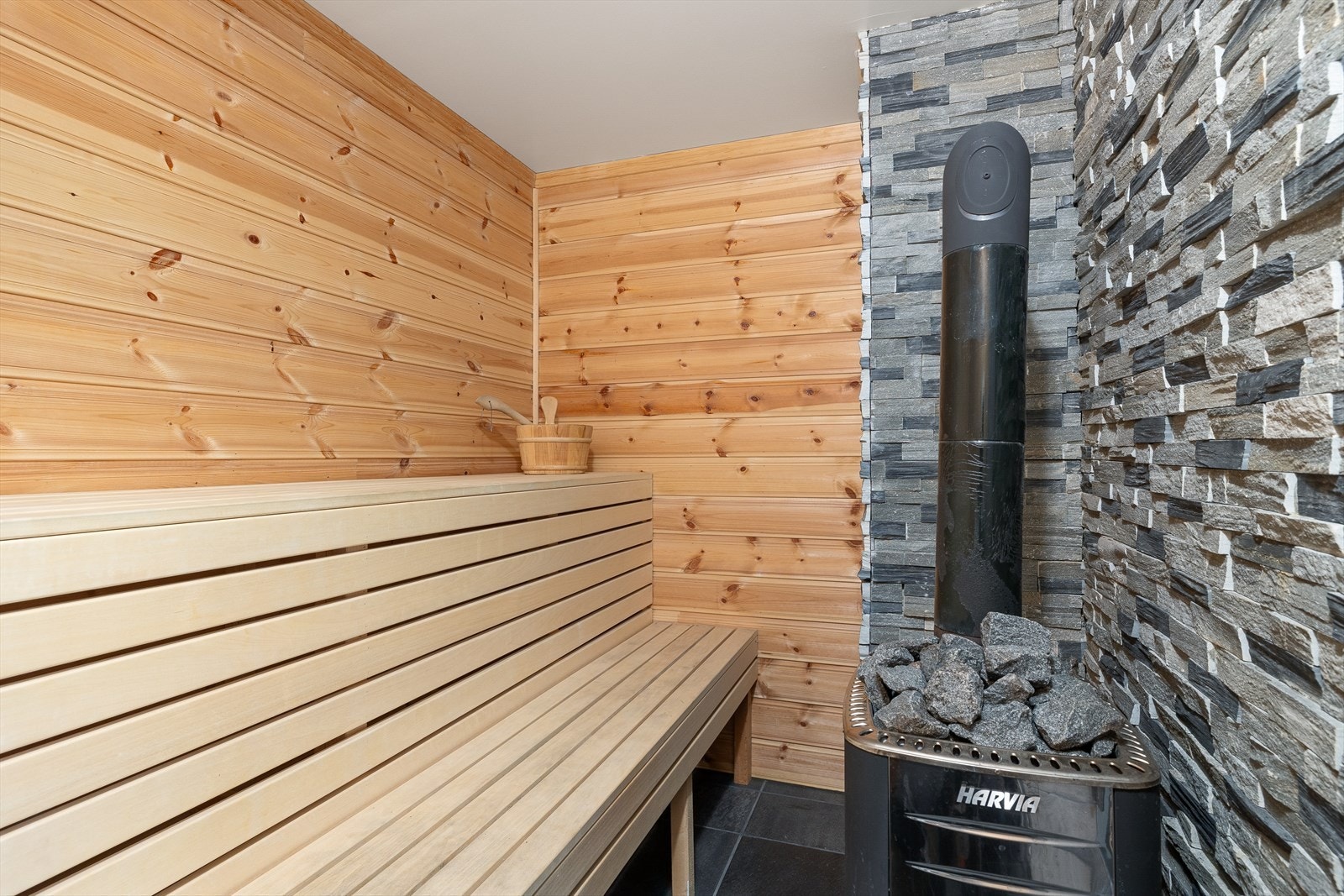 Plassbygd badstue med flis på gulv og panel på vegger (pipe/brannmur med limt skifer). Tak har malte plater. Benker. Vedfyrt ovn. Veggventil. Galleribilde