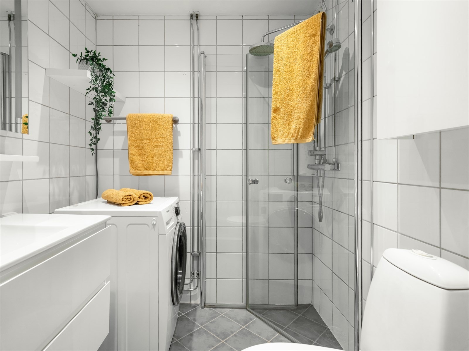 Pent flislagt bad med hjørnedusj, servant med underskap og speil. Det er opplegg for vaskemaskin. Galleribilde