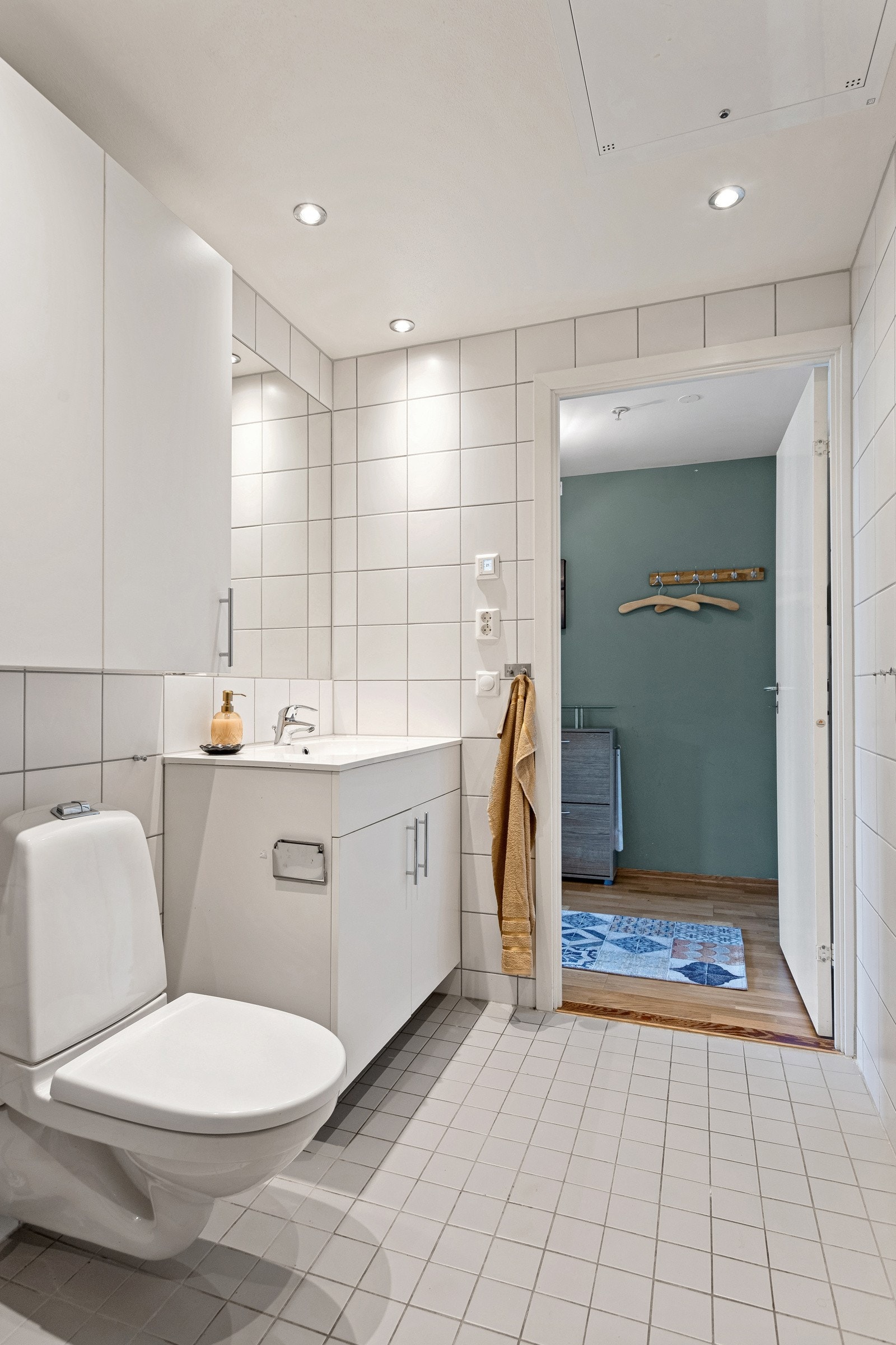 Badet er utstyrt med dusj, heldekkende servant med underskap, innfliset speil, veggskap og wc. Galleribilde