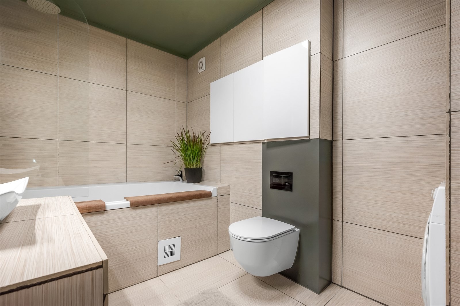 Badet er utstyrt med servantinnredning, servant, speil med belysning over, stikkontakt, vegghengt klosett fra 2019 og innmurt badekar med veggmontert armatur, garnityr og dusjvegg. Galleribilde