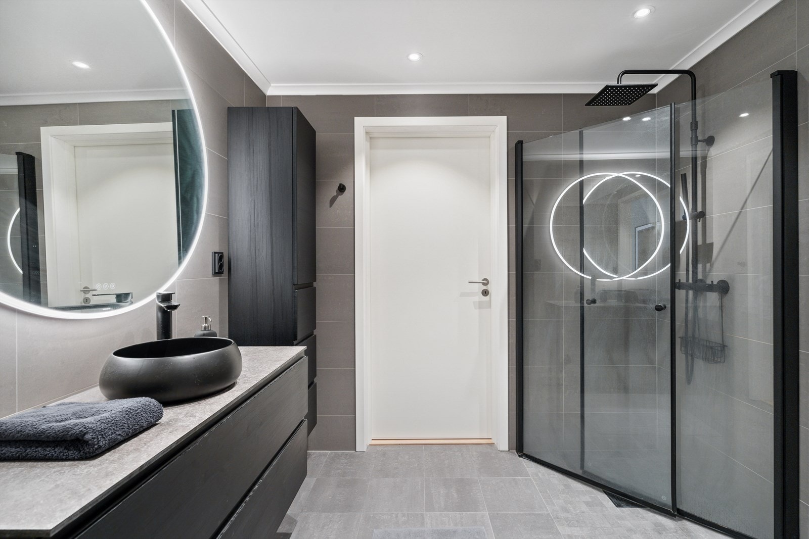 Påkostet baderom med fliser på gulv med varmekabler, flislagte vegger og malte slette plater med downlights i innvendig tak. Galleribilde