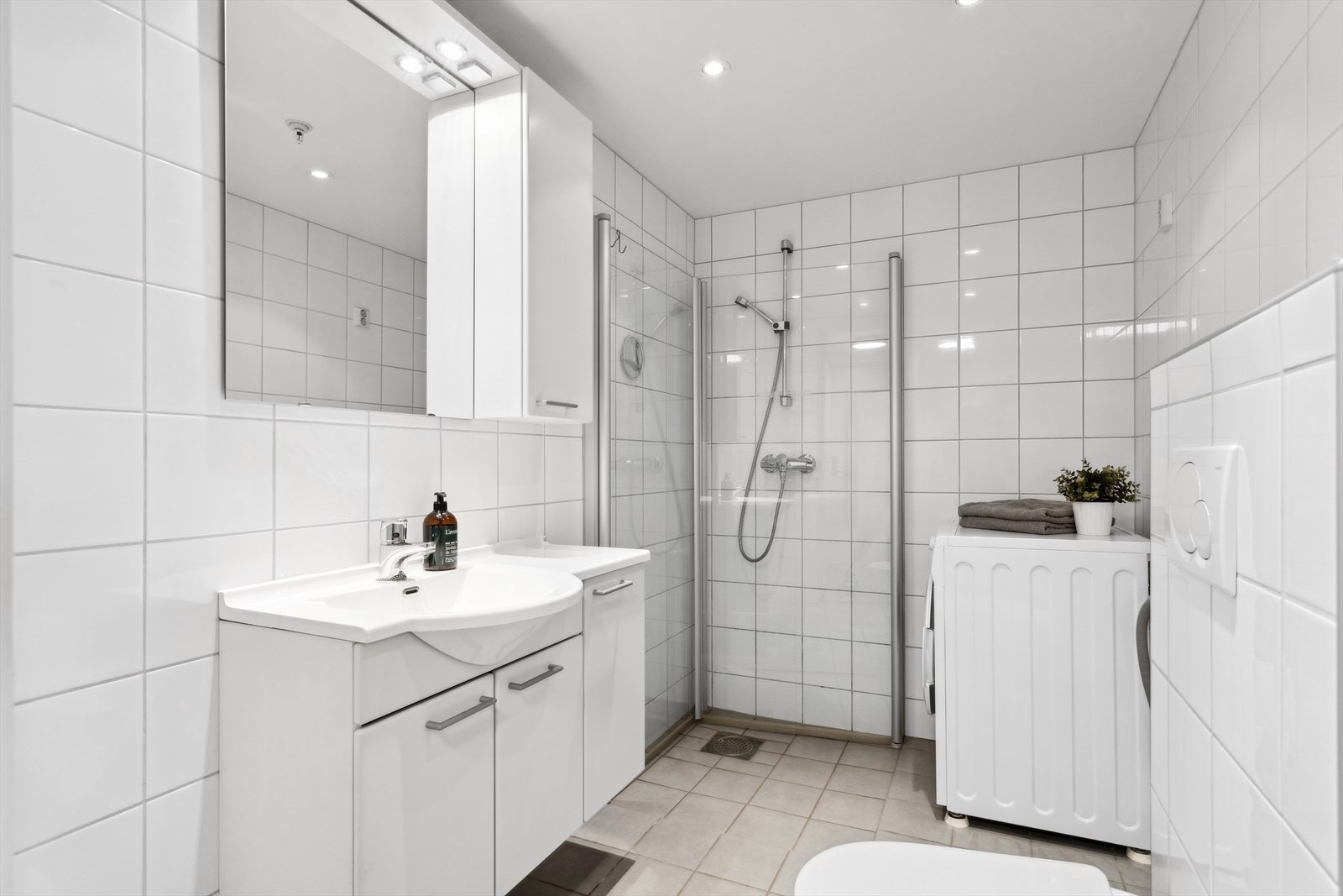 Badet har dusjvegger av glass, vegghengt toalett, innredning med servant samt opplegg for vaskemaskin. Galleribilde