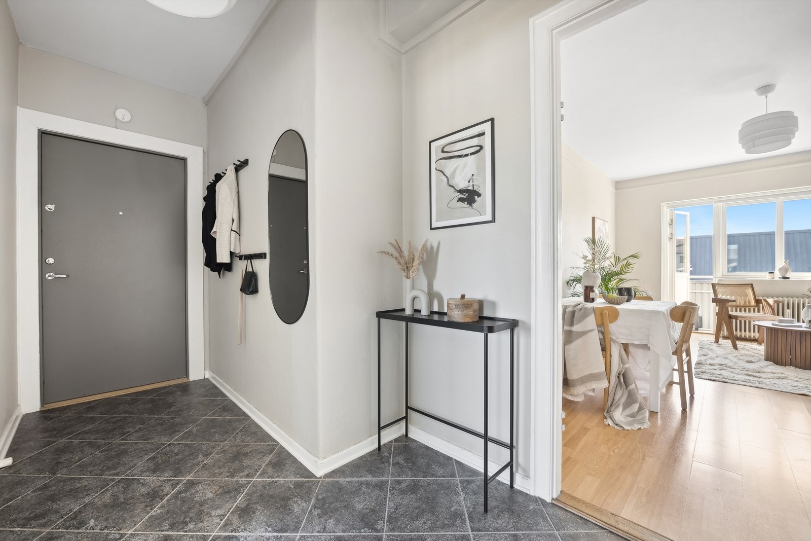 Lys og innbydende entré med veggflater som er malt opp i en delikat gråtone, mens gulvflatene består av mørke fliser Galleribilde