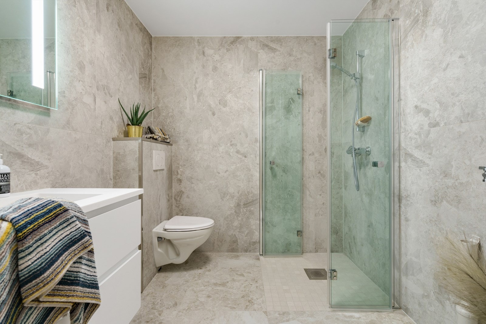 Det minste badet er utført med moderne store fliser på både gulv og vegger (vannbåren gulvvarme). Rommet er utstyrt med dusjnisje m/glassvegger, vegghengt toalett og baderomsinnredning Galleribilde