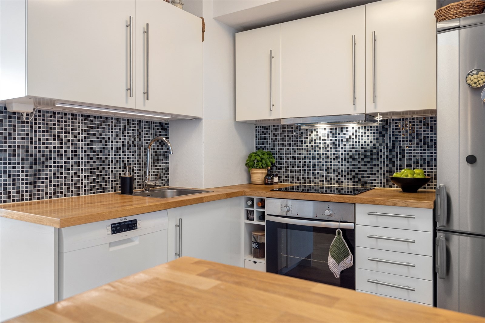 Lys innredning med glatte fronter, flis på vegg over kjøkkenbenk og heltre benkeplate Galleribilde