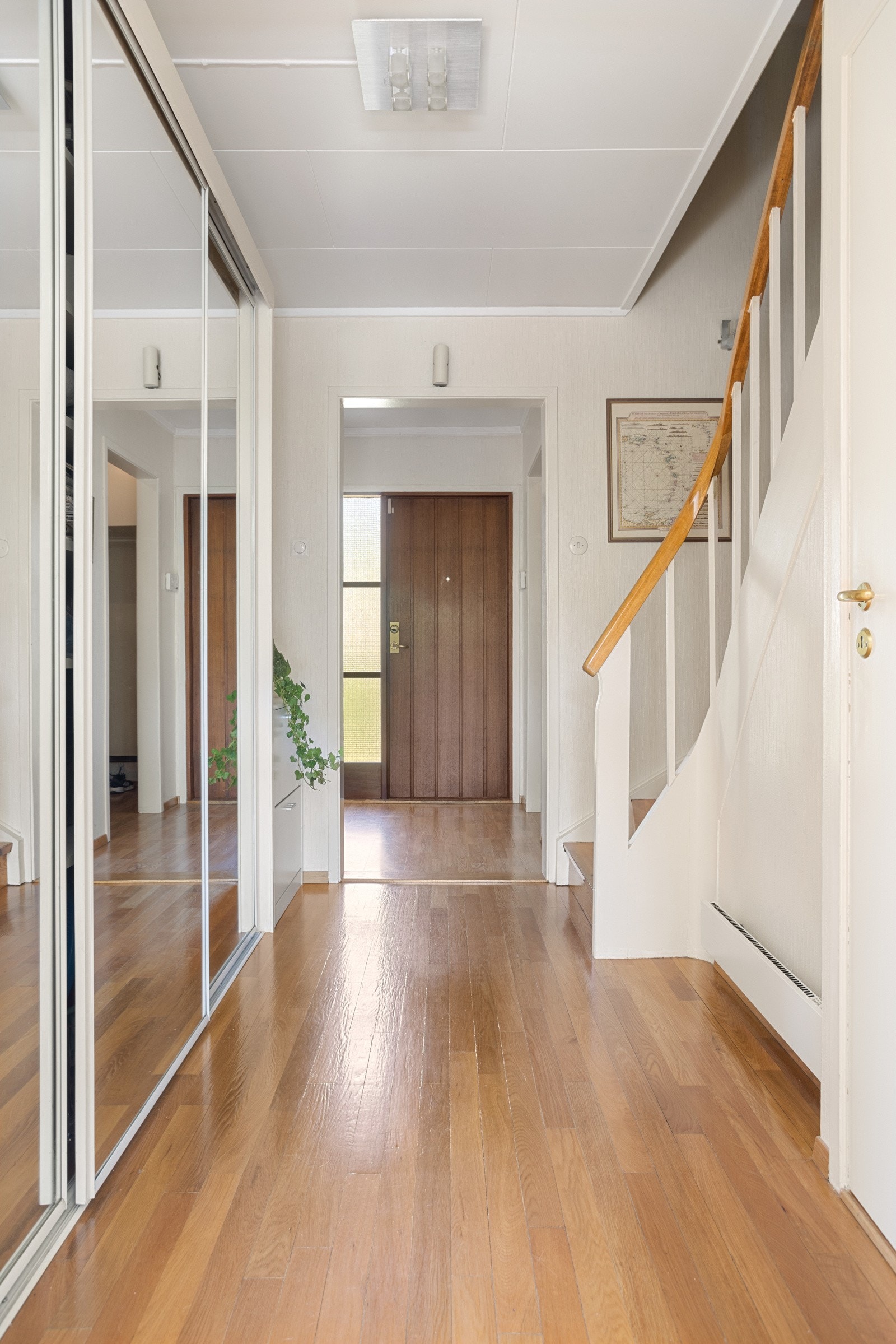 Vel inne blir vi ønsket velkommen i en lys og fin entré med hvitmalte vegger mot gyllent parkettgulv Galleribilde