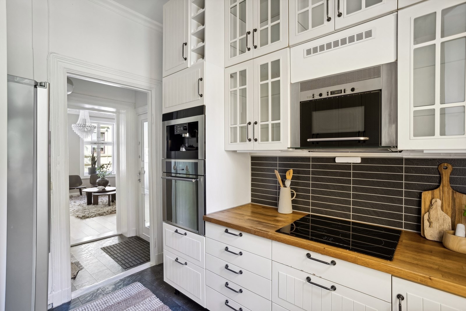 Kjøkkeninnredning fra 2010 med hvite profilerte fronter, flere overskap med fronter i glass og benkeplater i heltre. Galleribilde