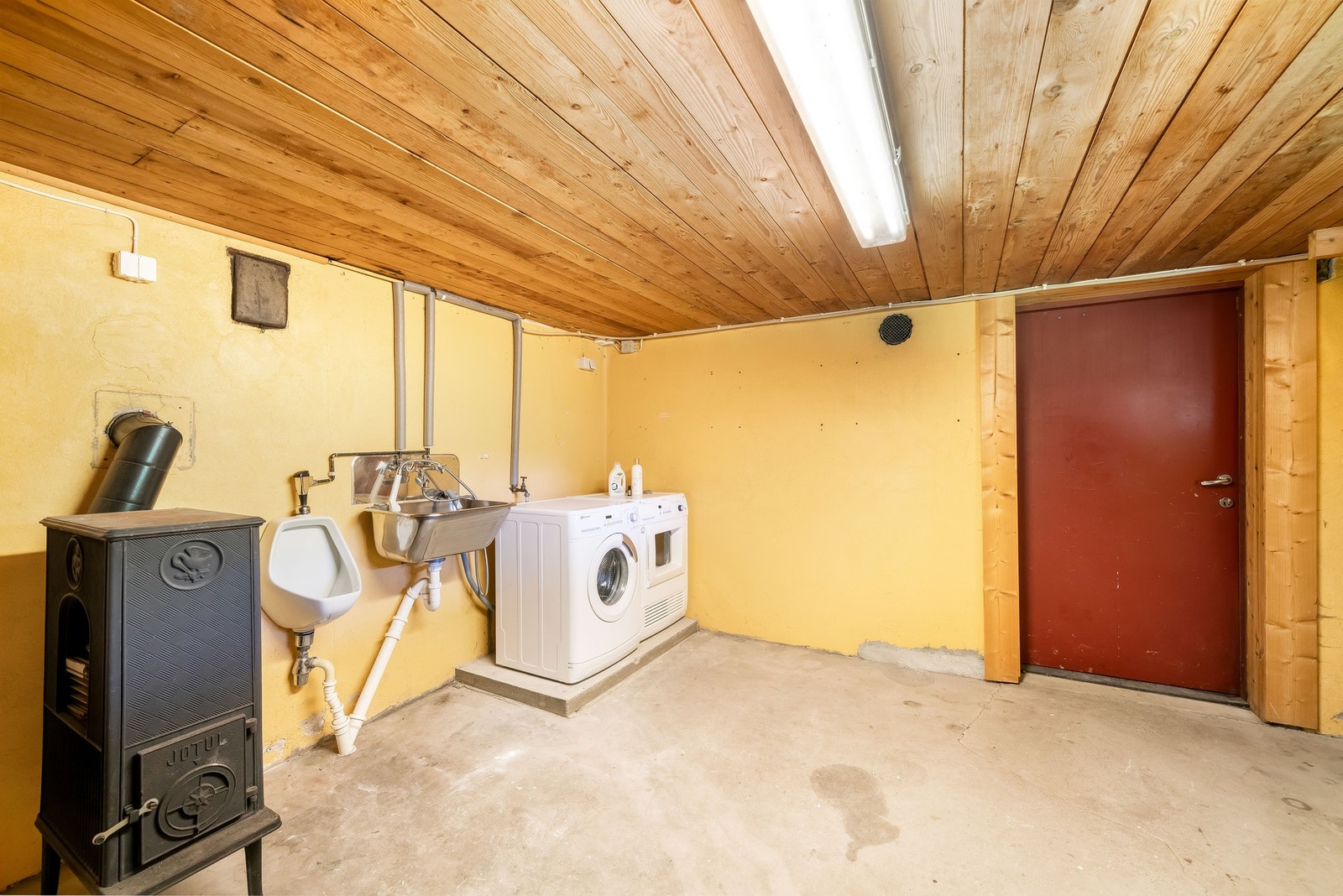 Vaskerom i kjelleren med vedovn og pissoar. Her kan man innrede til treningsrom eller forlenge hobbyverkstedet fra garasjen. Kanskje man behøver ett samlingssted til hobbykvelder? Galleribilde