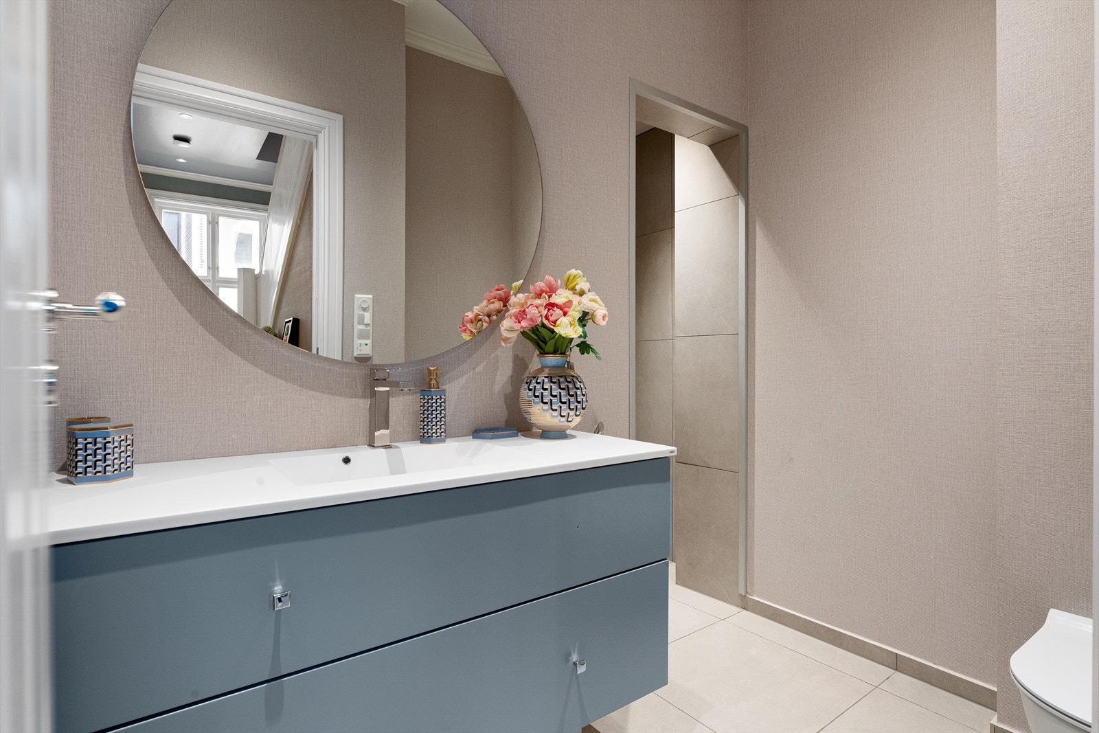 Moderne og stilfullt bad fra 2020 med bemerkelsesverdig takhøyde (ca. 2,89m) og dimmerstyrte downlights i himling. Våtromstapet på vegger og fliser på gulvet med varmekabler. Veggmontert wc, servant i innredning fra danske Kuma samt speil i rommet. Galleribilde