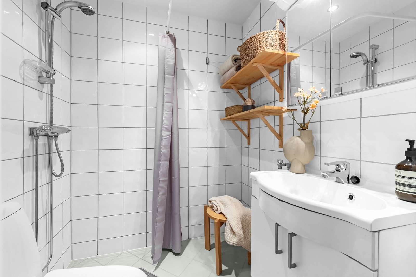 Lyst baderom fra 2004. Baderomsinnredning i hvit glatt utførelse med servant og ett-greps bl. batteri, speilskap og lys. Dusjhjørne med forheng og gulvstående toalett. Opplegg for vaskemaskin Galleribilde