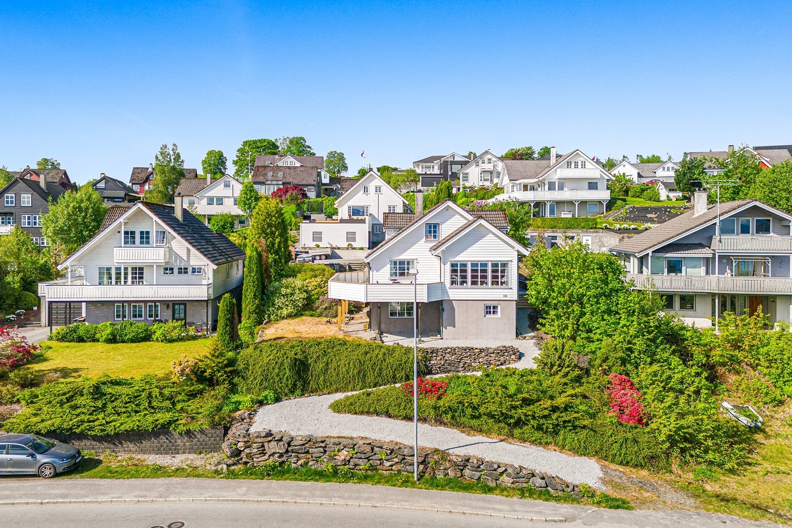 Parkeringsareal med oppstillingsplass for flere biler på overside av boligen og egen oppstillingsplass på nedside av hus for utleiedel med gangsti til inngangsparti. Galleribilde