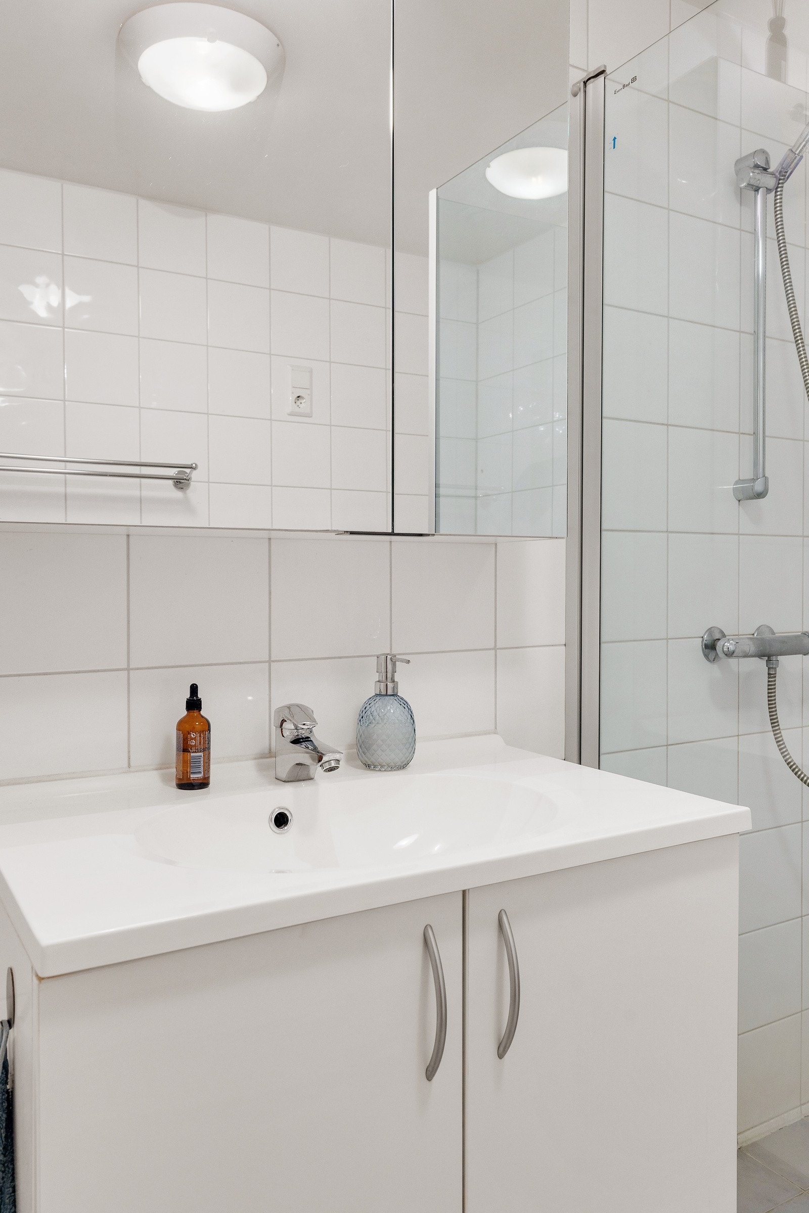 Badet inneholder vegghengt innredning med heldekkende servant, speilskap, vegghengt wc og dusjhjørne med innfellbare dører i glass. Galleribilde