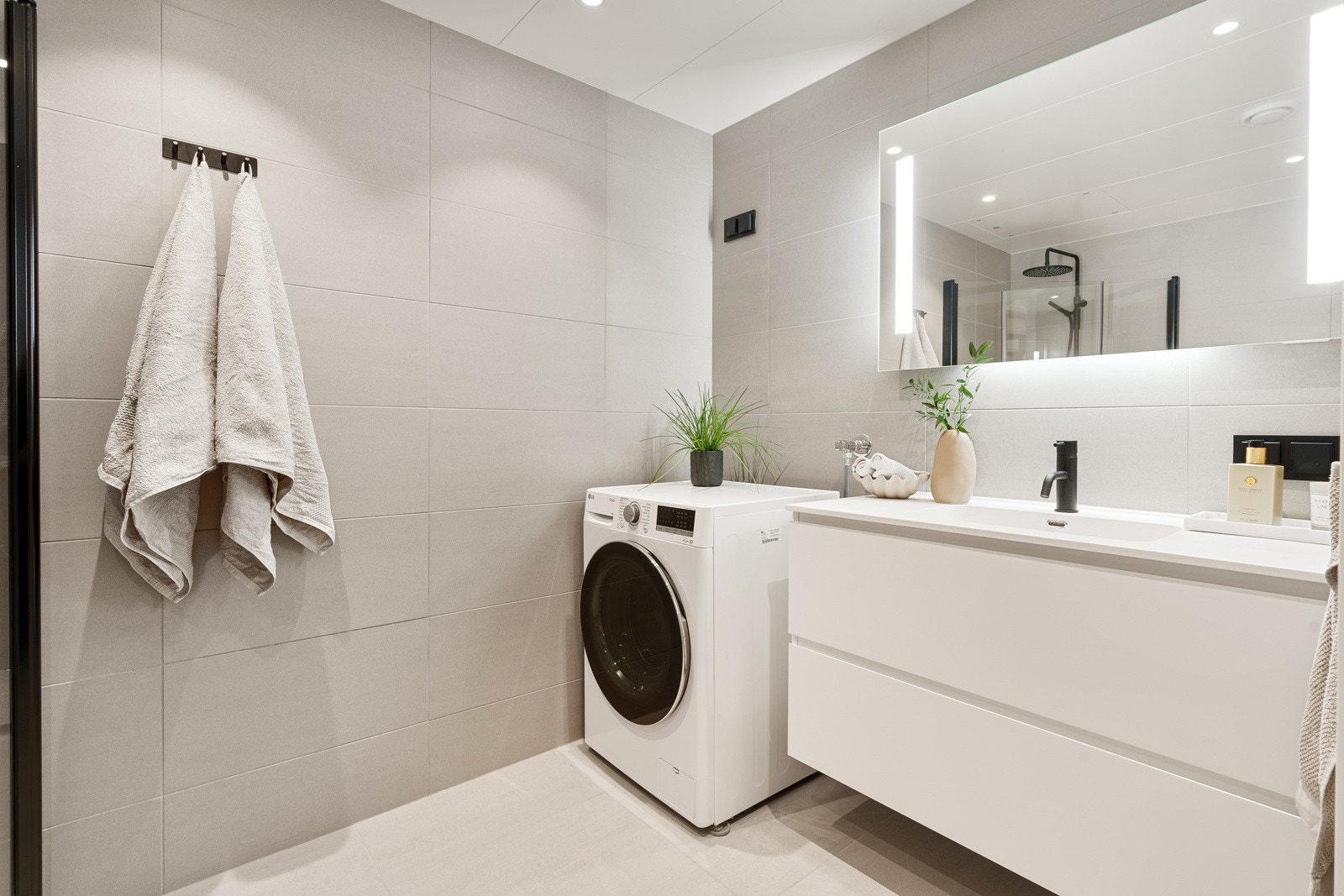 Moderne og flislagt bad med vegghengt wc og opplegg for vaskemaskin og plass for tørketrommel. Innredning med gode oppbevaringsmuligheter og speil med belysning. Galleribilde