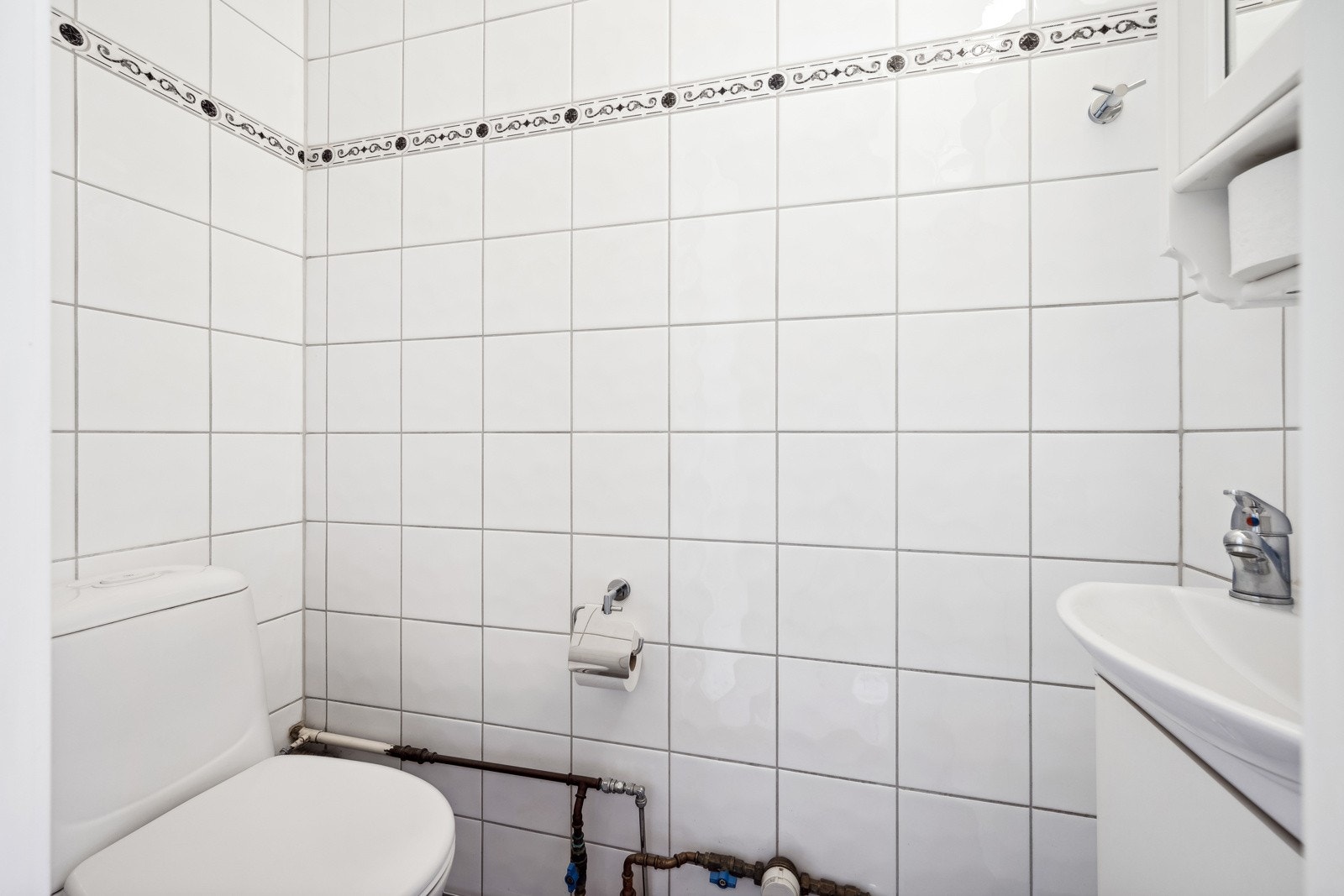 Flislagt toalettrom med underskap og heldekkende servant med ettgreps blandebatteri. Vegghengt speilskap med belysning over servant. Galleribilde