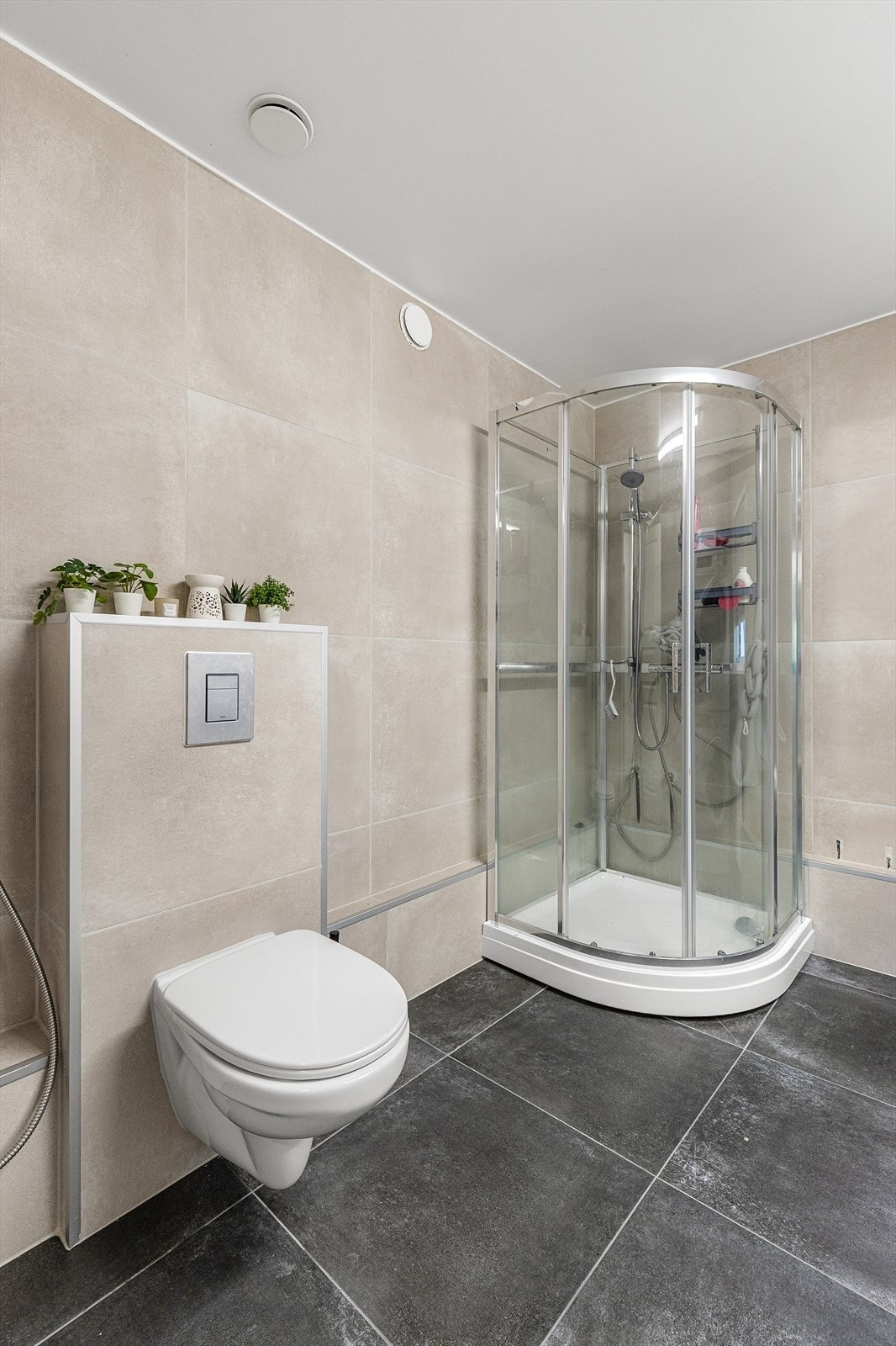 Badet er utstyrt med vegghengt toalett, dusjkabinett, vegghengt speilskap og vegghengt servantinnredning med skuffer og ovenpåliggende servant. Galleribilde