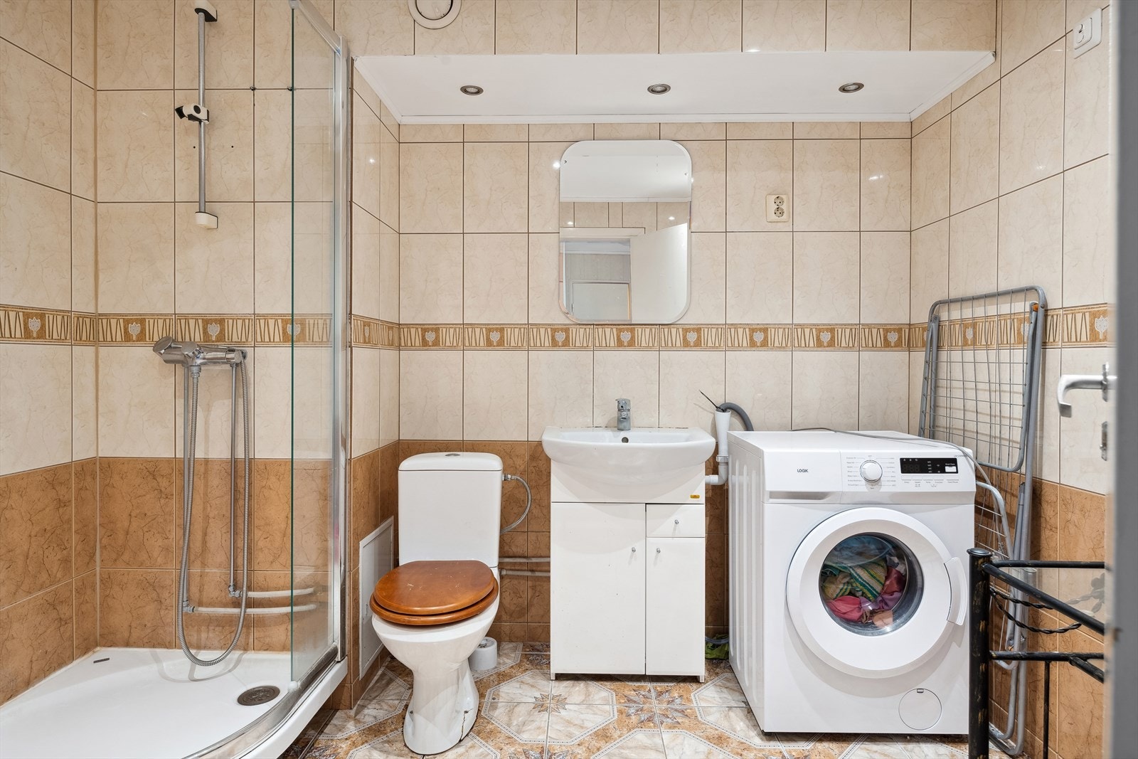 Det romslige badet har god omkledningsplass. Her er det nedfelt tak ved innredning med downlights. Det er varmekabler i gulv. Innredning, wc og dusj med noe skade. Galleribilde