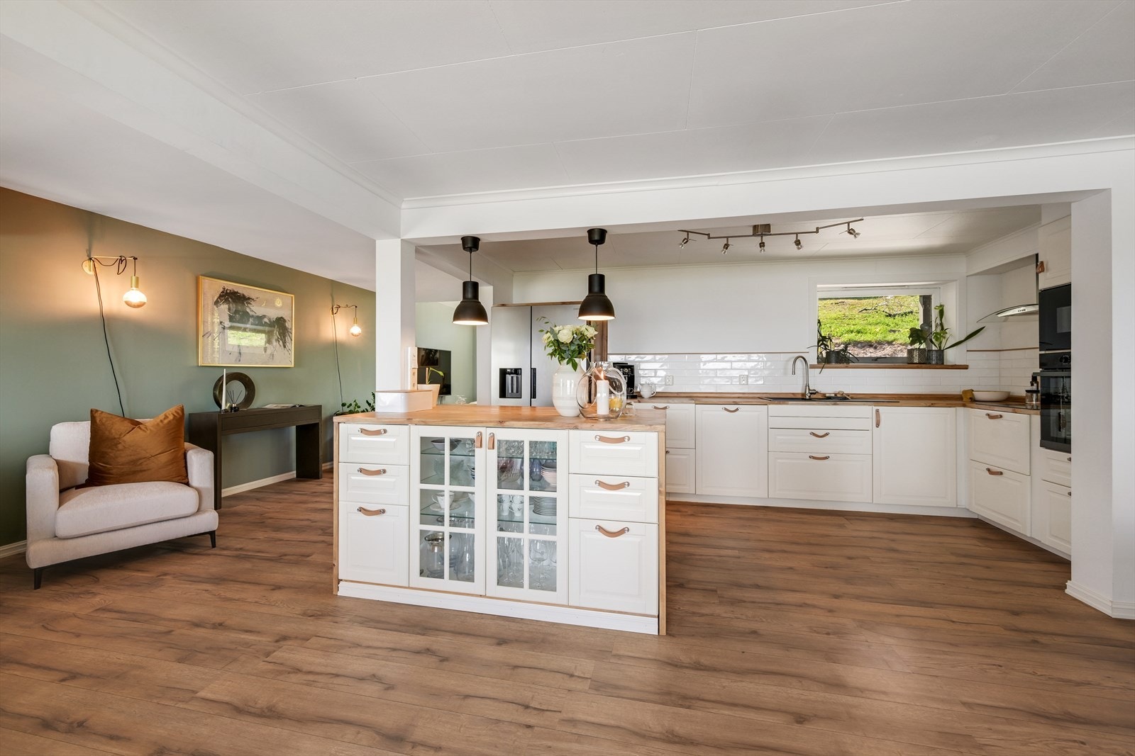 Kjøkken med fliser på vegg over benk, kjøkkenøy som deler av fra stuer. Galleribilde