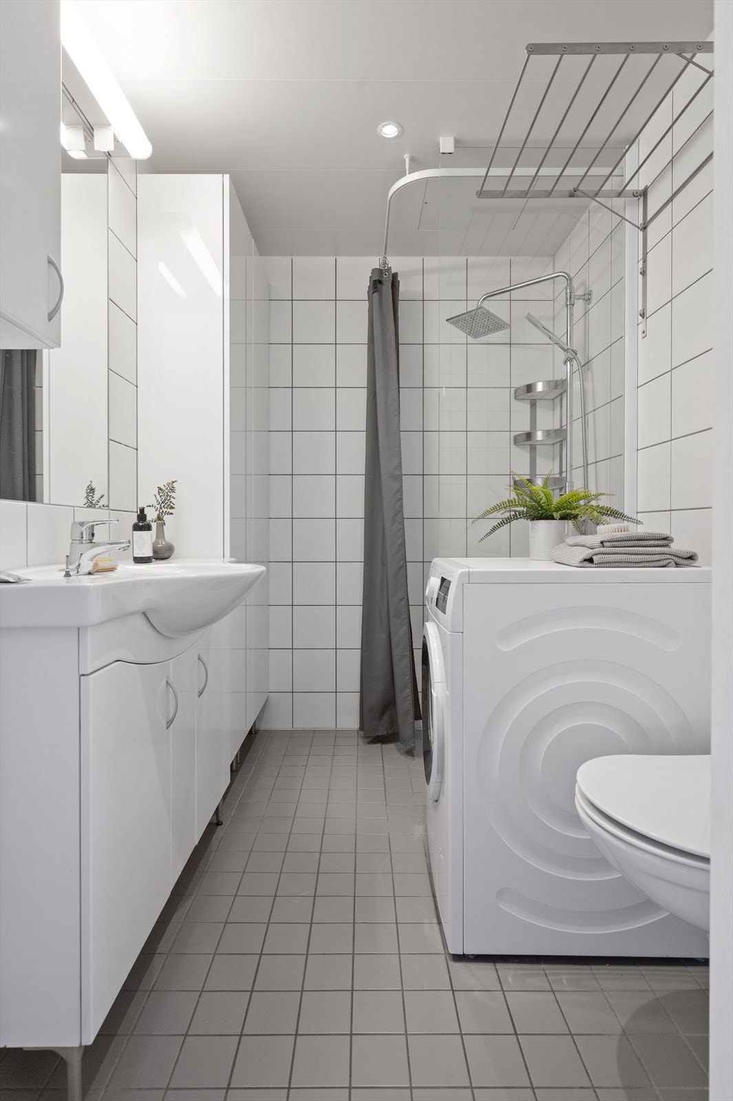 Badet er innredet med vegghengt servantskap, servant, vegghengt speil med overbelysning, dusjhjørne med glassvegg, regndusj og hånddusj, vegghengt toalett med innebygget sisternekasse. Galleribilde