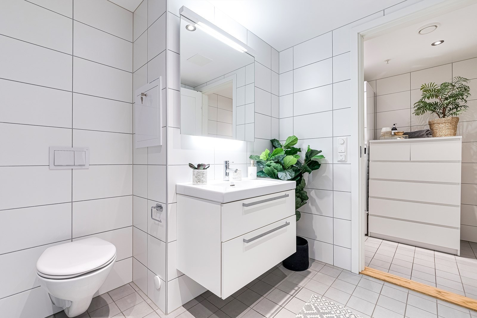 Badet er innredet med dusj på gulv med dører i herdet glass, veggfestet klosett med innebygget sisterne og servant i helstøpt plate. Galleribilde