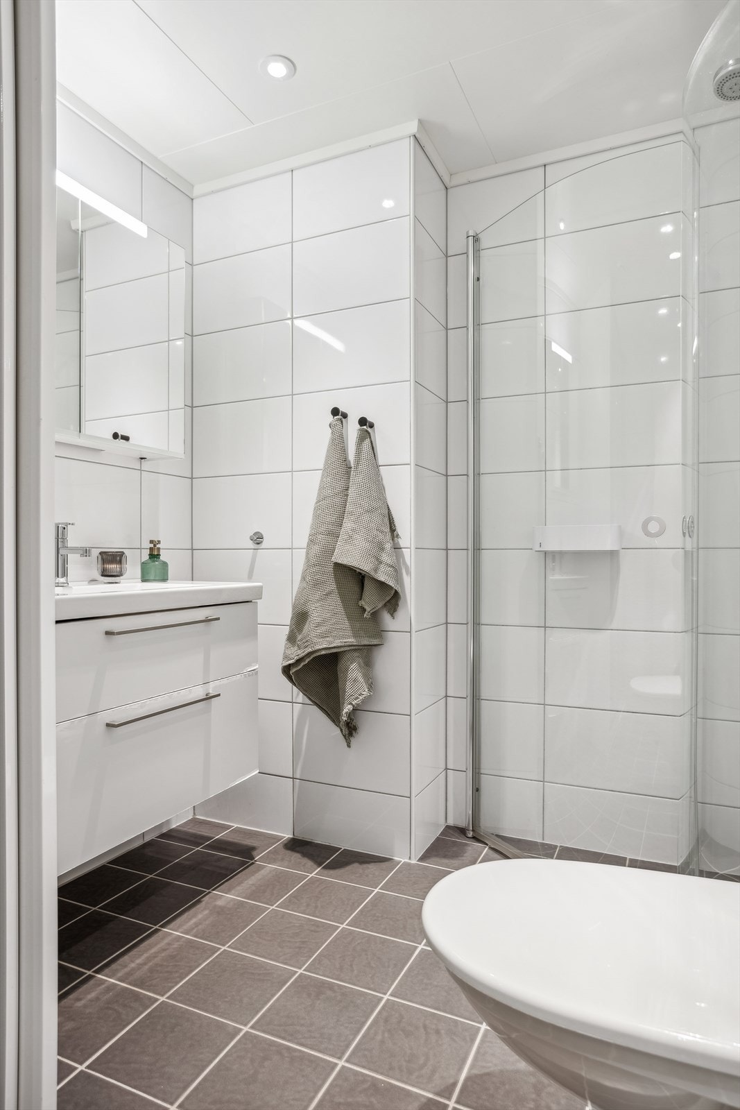 Badet har dusjhjørne med svingbare glassdører, vegghengt toalett, baderomsmøblement med heldekkende servant og speilskap med lys. Galleribilde
