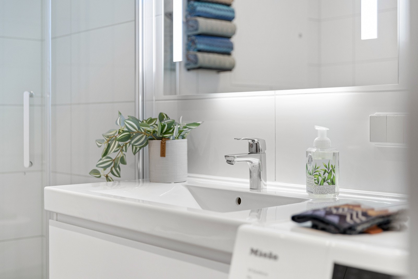 Innredet med dusjhjørne med regnfallsdusj, vegghengt toalett, speil med belysning og servant med underskap. Galleribilde