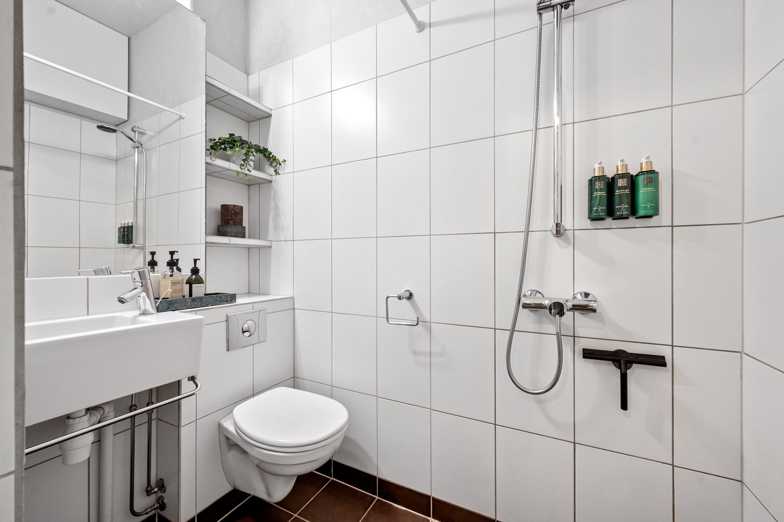 Baderom med gulvvarme pusset opp i 2005. Badet er innredet med veggmontert servant, speil over servant og belysning på vegg, dusj på vegg med ett-greps armatur, vegghengt toalett med innebygget sisterne fra Grohe Galleribilde