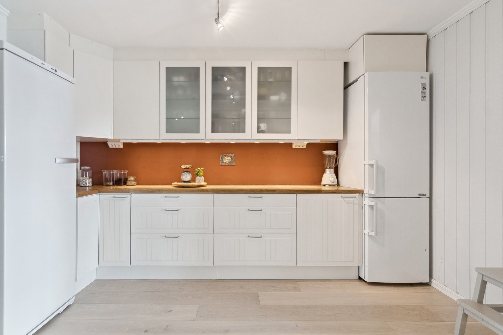 Kjøkkenet er innredet med hvite glatte fronter, benkeplate av heltre og fliser over benk. Galleribilde