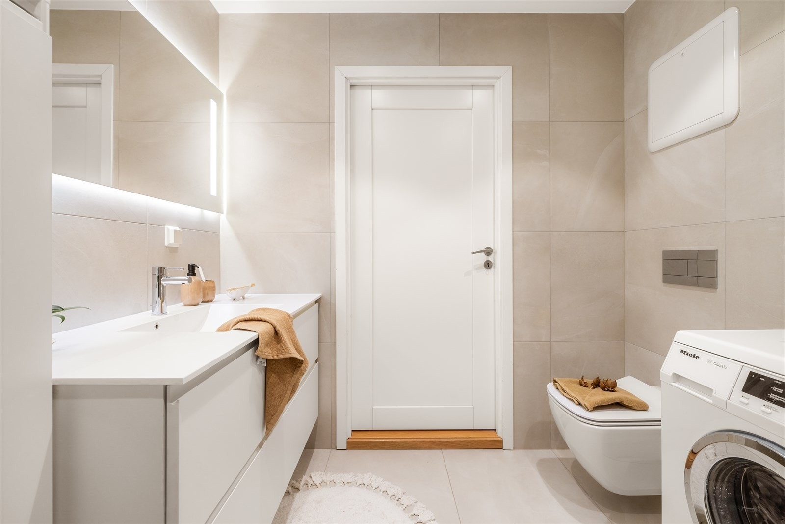 Badet inneholder servant i møblement, speil med belysning, dusjhjørne med dører i glass og vegghengt toalett. Galleribilde