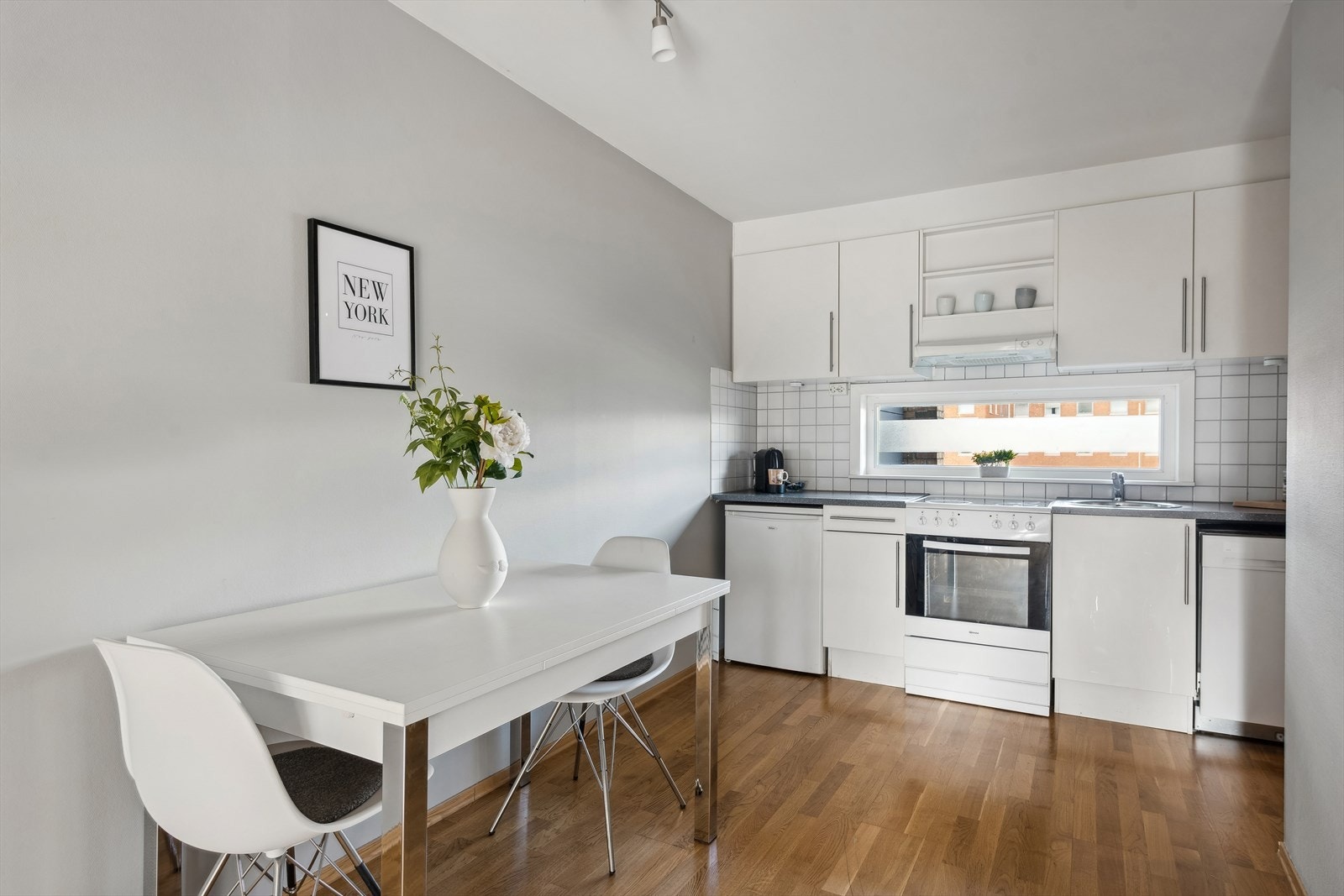 Lyst og enkelt kjøkken med benke- og overskap med slette fronter, laminat benkeplate, og fliser på veggen over benken. Galleribilde