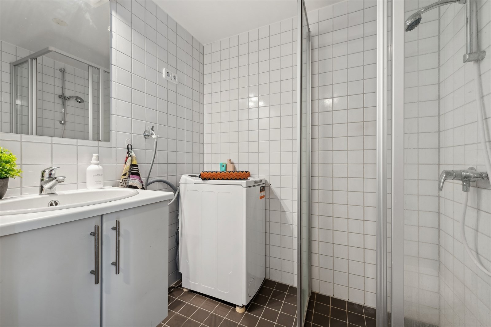 Flislagt baderom med dusjhjørne utstyrt med to skyvbare glassdører og vegghengt toalett. Galleribilde