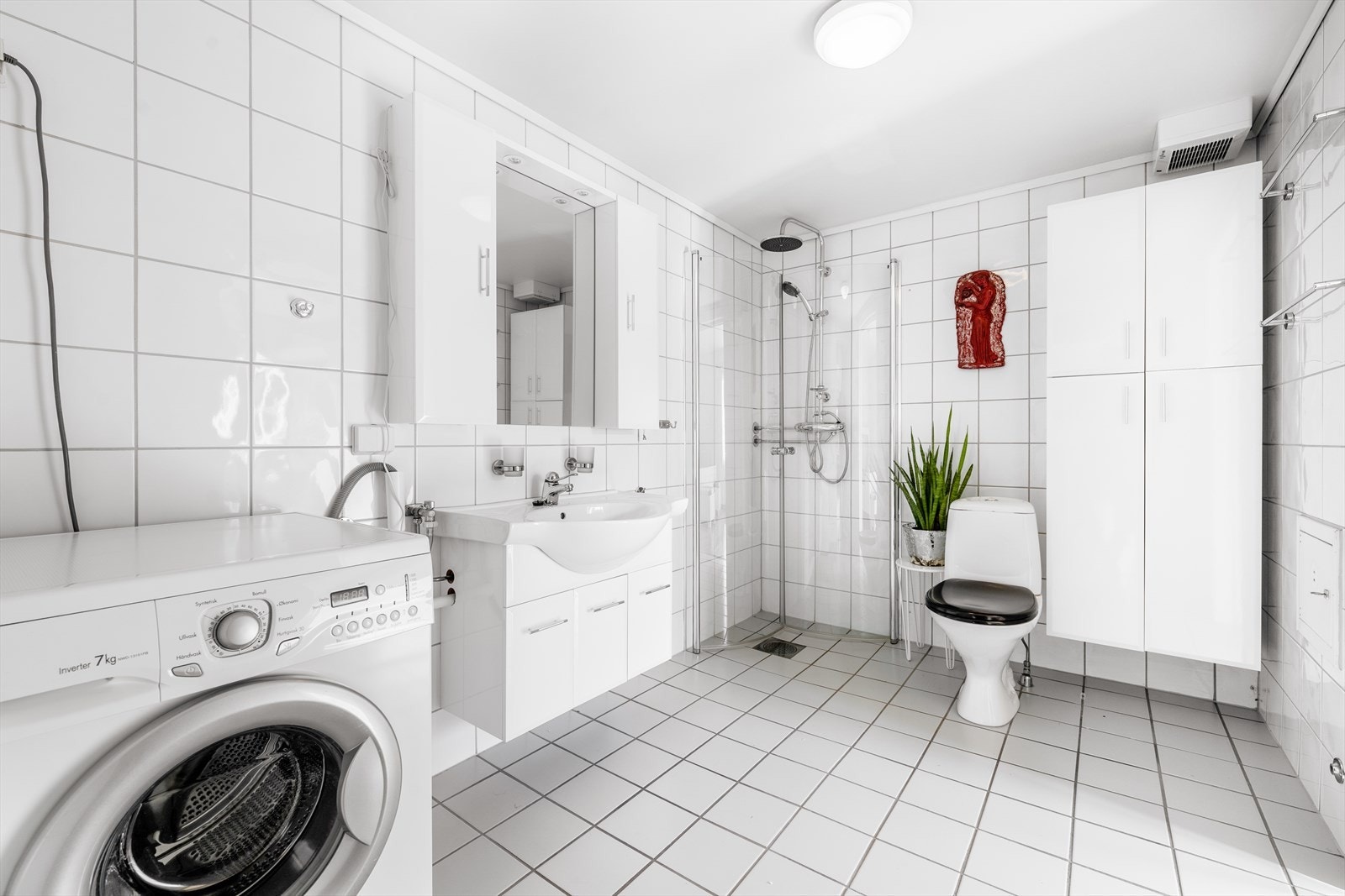 Flislagt bad med varmekabler i gulv. Badet er innredet med toalett, dusjhjørne og servantinnredning med underskap, overskap og speil med overlys. Samt veggmonterte skap. Det er opplegg for vaskemaskin. Galleribilde