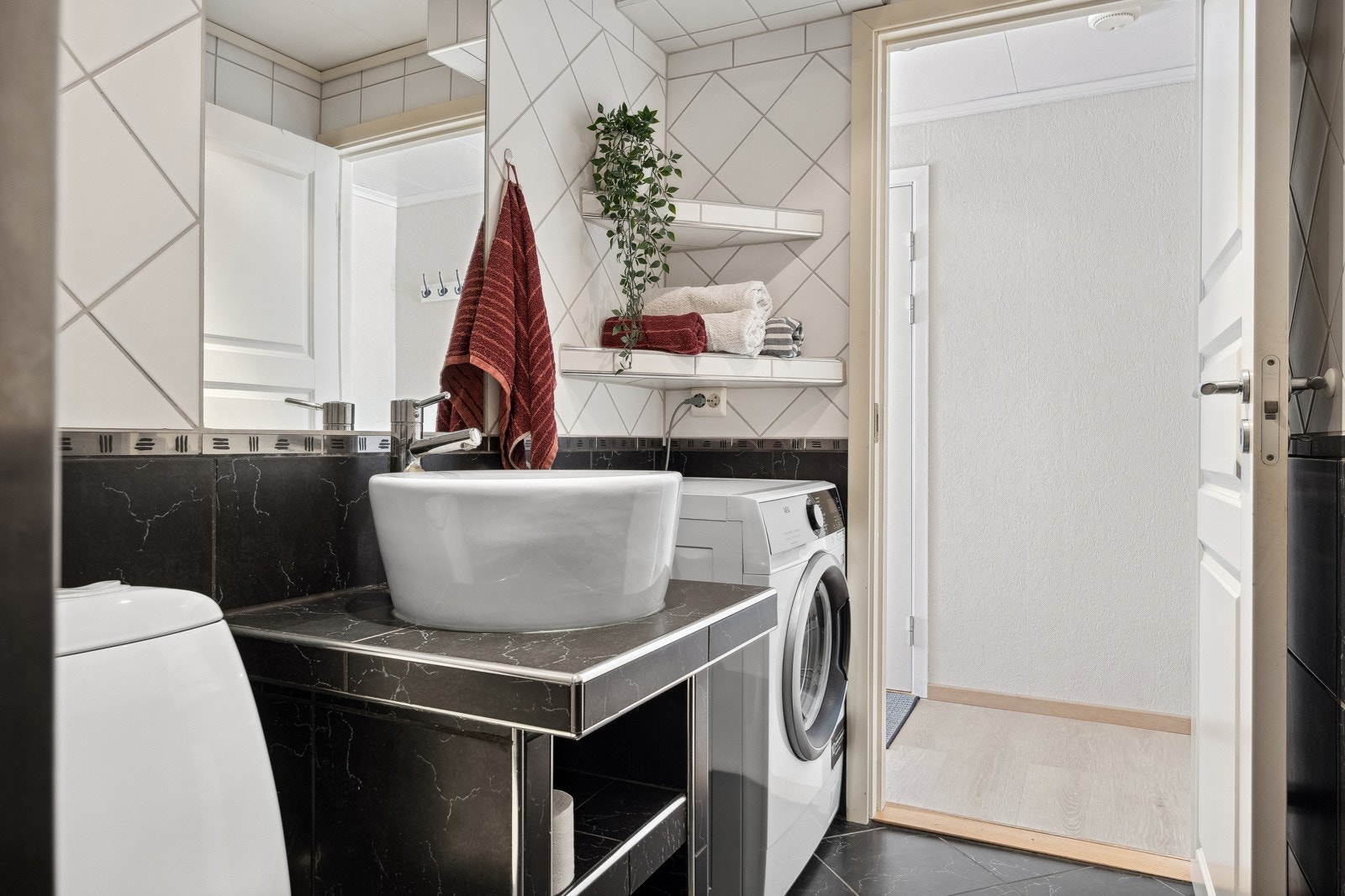 Badet måler 3,5 kvm og er utstyrt med dusjnisje, overliggende servantskål, hyller til oppbevaring, speil, toalett og opplegg for vaskemaskin. Galleribilde