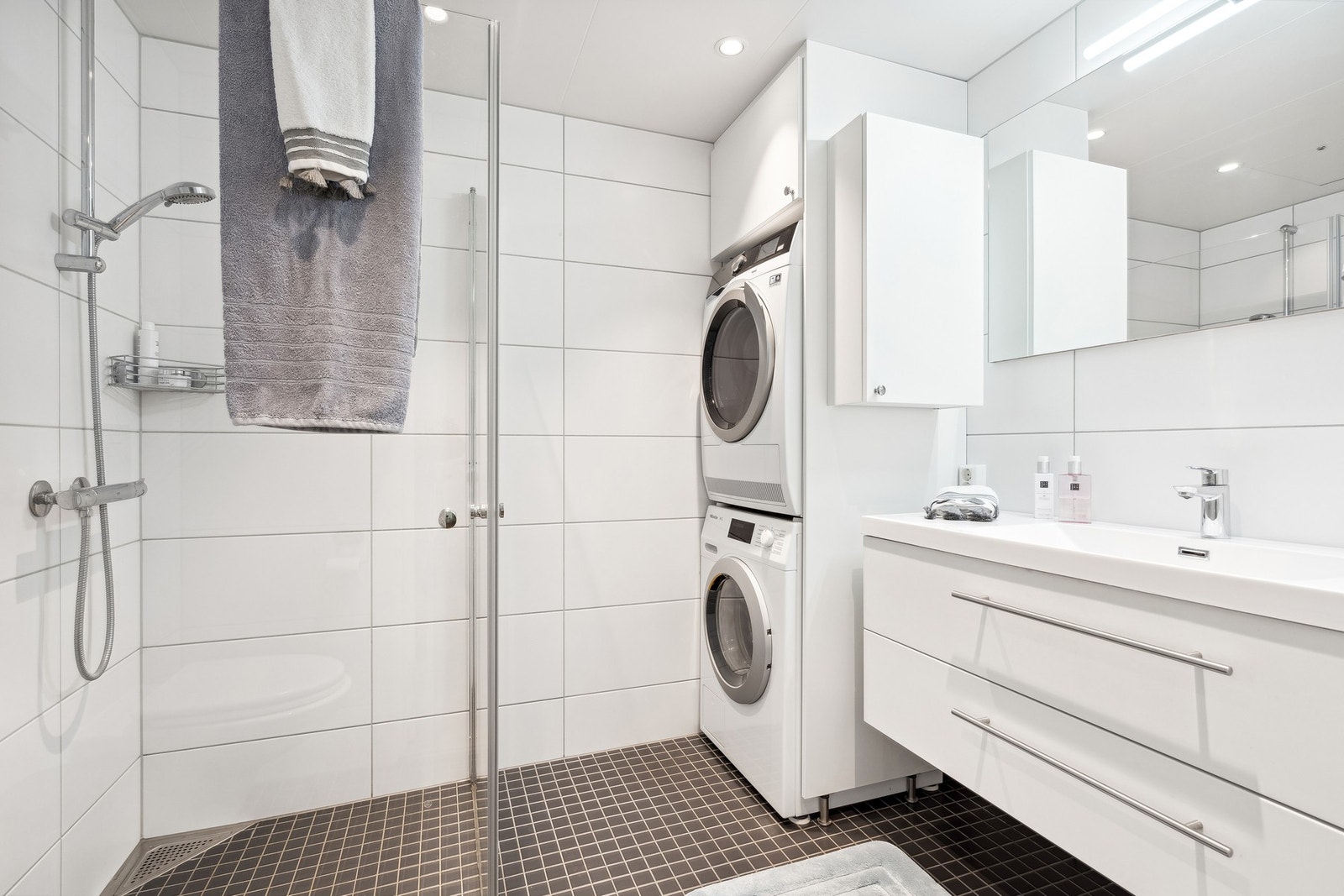 Baderommet er innredet med servantplate på underskap og speilskap, noe som sikrer god oppbevaringsplass til baderomsartikler. Samt plassbesparende dusjdører i glass og kran/avløp til vaskemaskin. Galleribilde