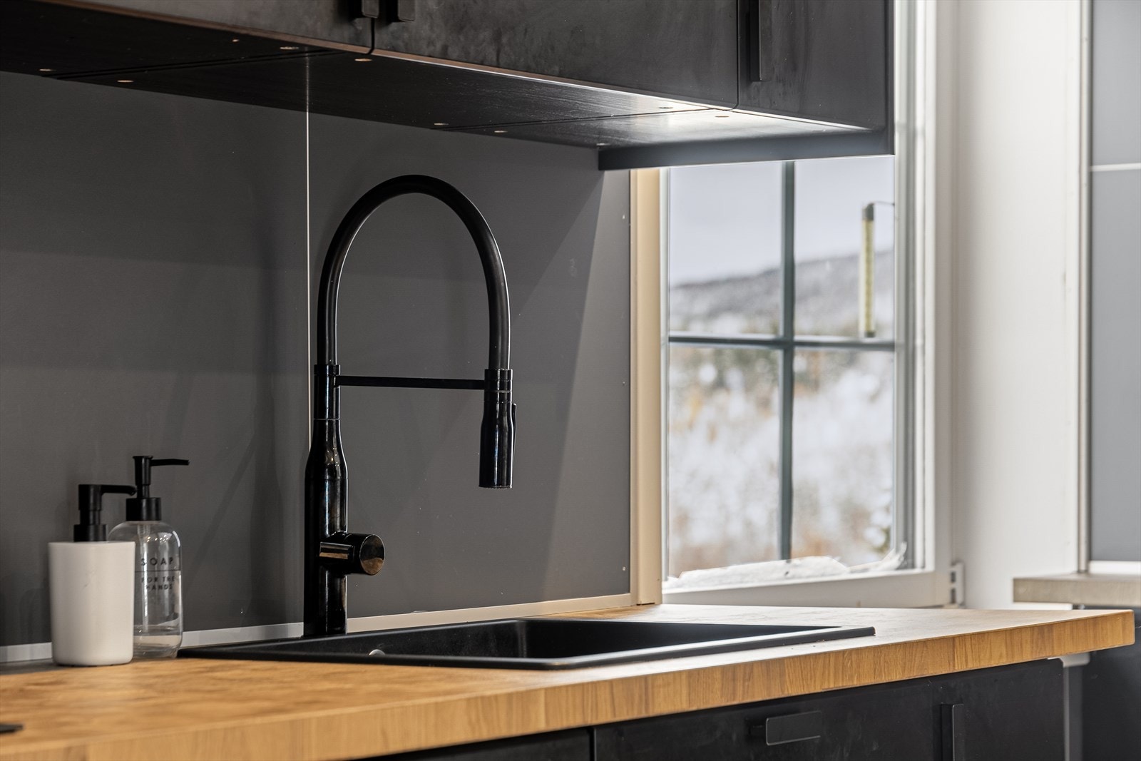 Svarte, stilfulle detaljer går igjen i hele rommet. Det er inngang til kjøkkenet fra to steder i stuen. Galleribilde