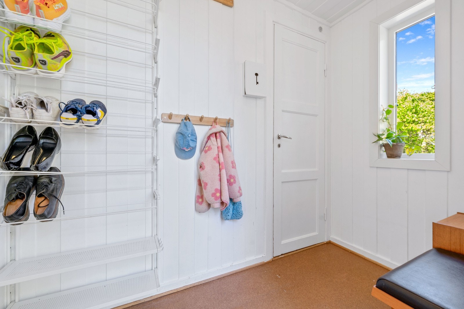Inngangsparti med lun hvitmalt panel på vegg og i himling. Plass til yttertøy og sko. Vindu vender mot inngangspartiet og det er dør som leder til kjelleren. Galleribilde