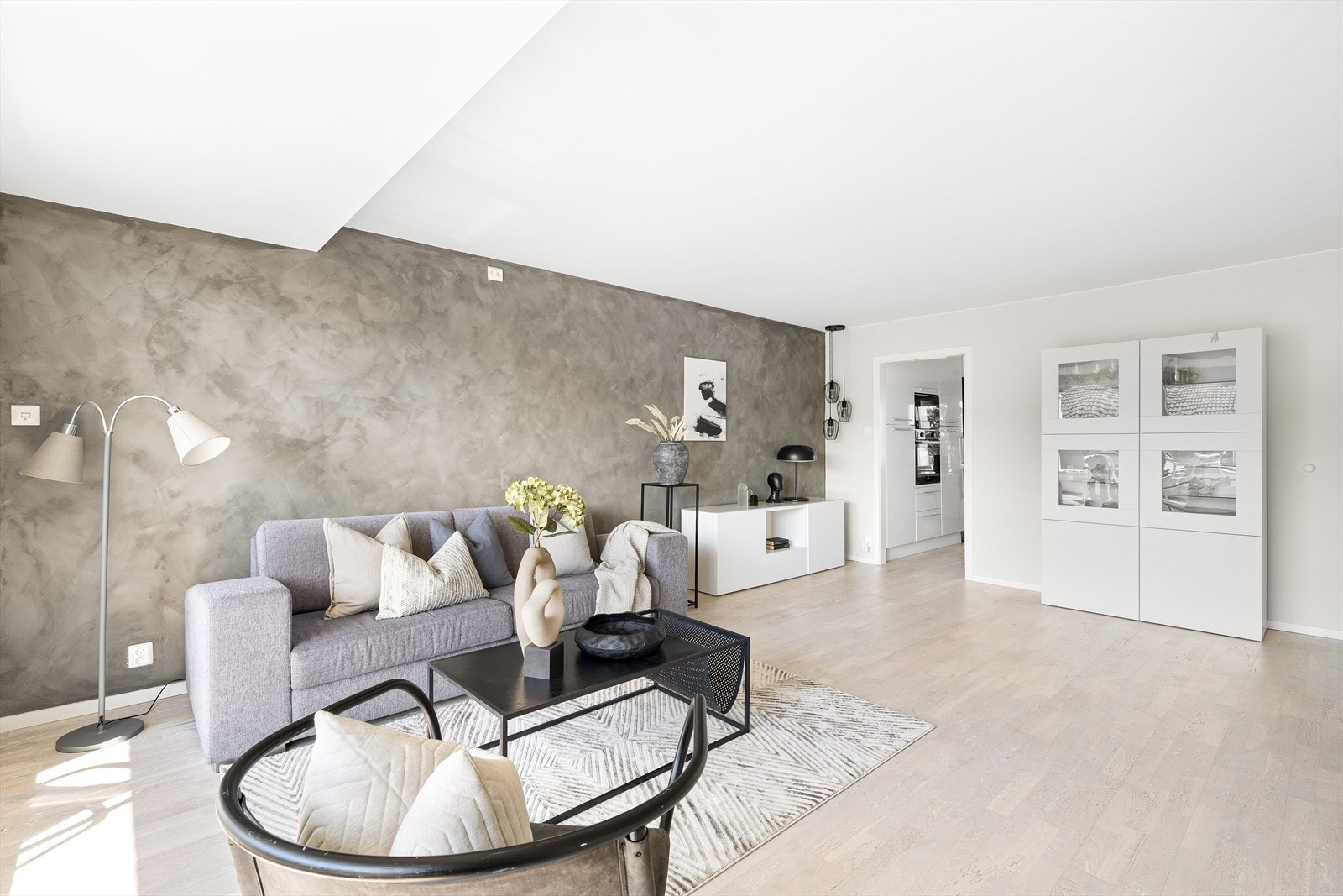 Romslig stue med flott kontrastvegg av mikrosement. 3-stavs parkett på gulv og listefritt mot tak. Galleribilde