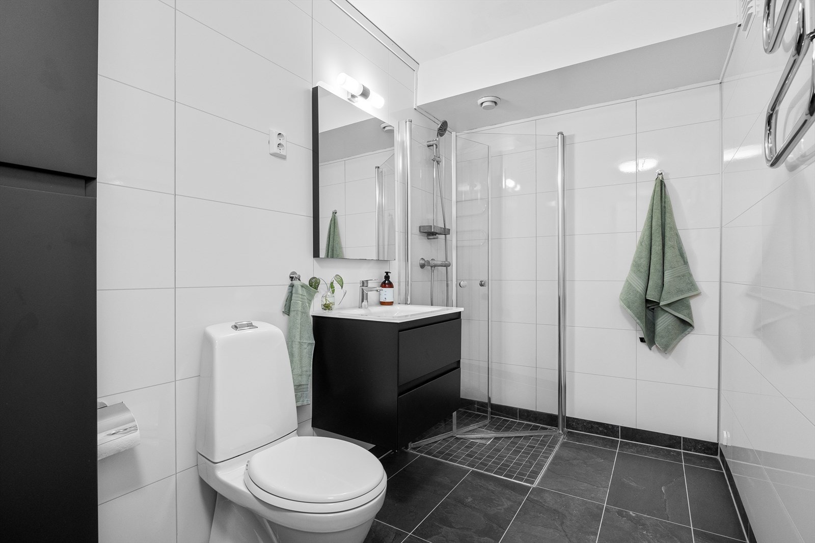 Badet er romslig og inneholder toalett, dusj med foldedører i glass, speil med belysning, baderomsinnredning med heldekkende servant og opplegg for vaskemaskin/tørketrommel Galleribilde