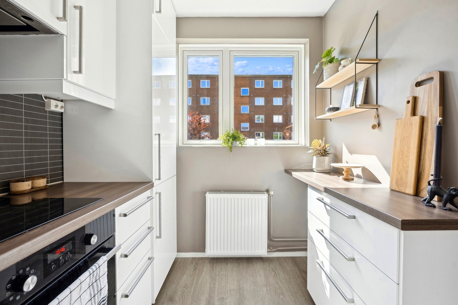 Veggflatene er malt opp i en smakfull og tidsriktig sandtone og man har mørke stilrene fliser mellom kjøkkenbenk og overskap Galleribilde