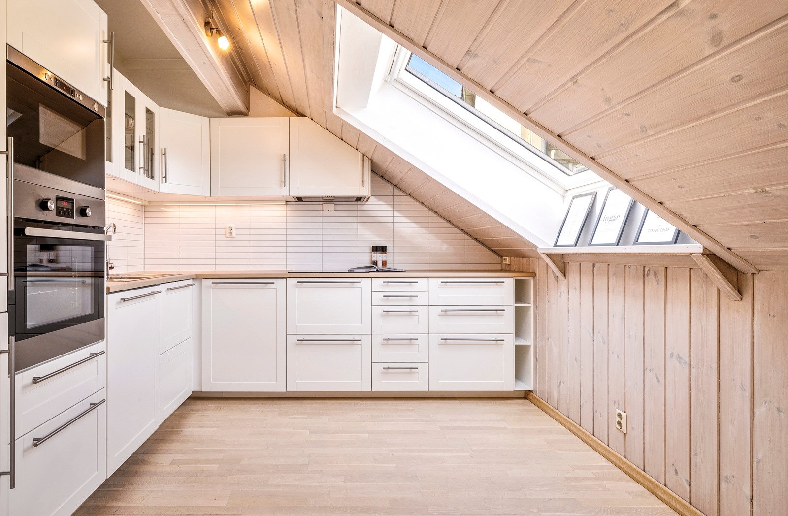 Kjøkkenet er innredet med hvite profilerte fronter, laminat benkeplate med nedfelt stål vaskebeslag. Mellom benk og overskap er det satt opp Kitchen-board Galleribilde