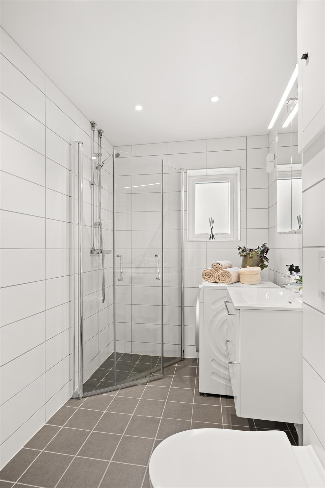 Badet har blant annet varmekabler i gulv, innfelte downlights, servant med oppbevaring og opplegg for vaskemaskin Galleribilde