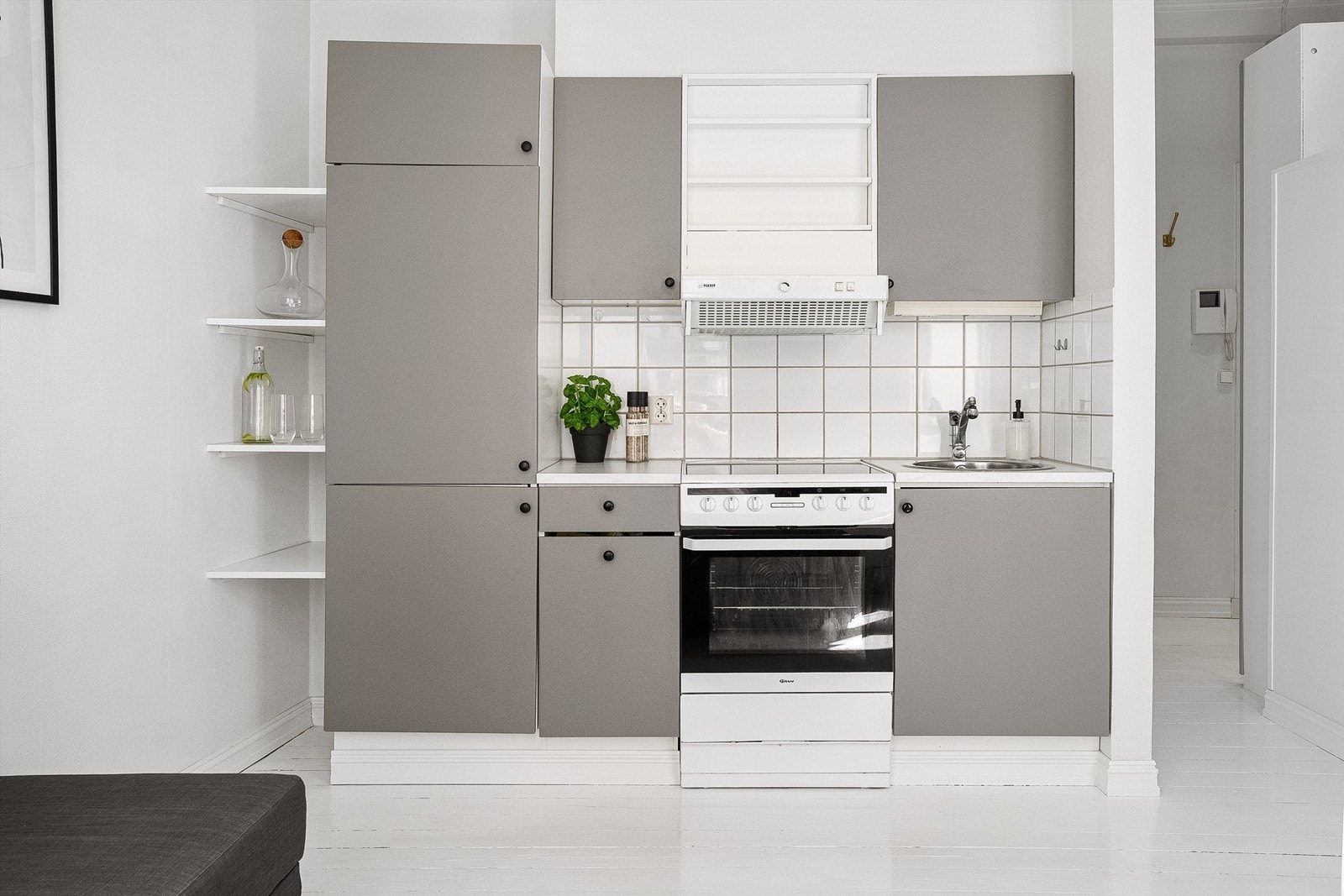 Kjøkken fra ukjent årstall med slette fronter og benkeplate av laminat. Det er nedfelt oppvaskkum med ett-greps kjøkkenarmatur, benkeskapsbelysning og stikkontakter over kjøkkenbenk, samt frittstående komfyr og integrert kjøleskap med fryser. Galleribilde