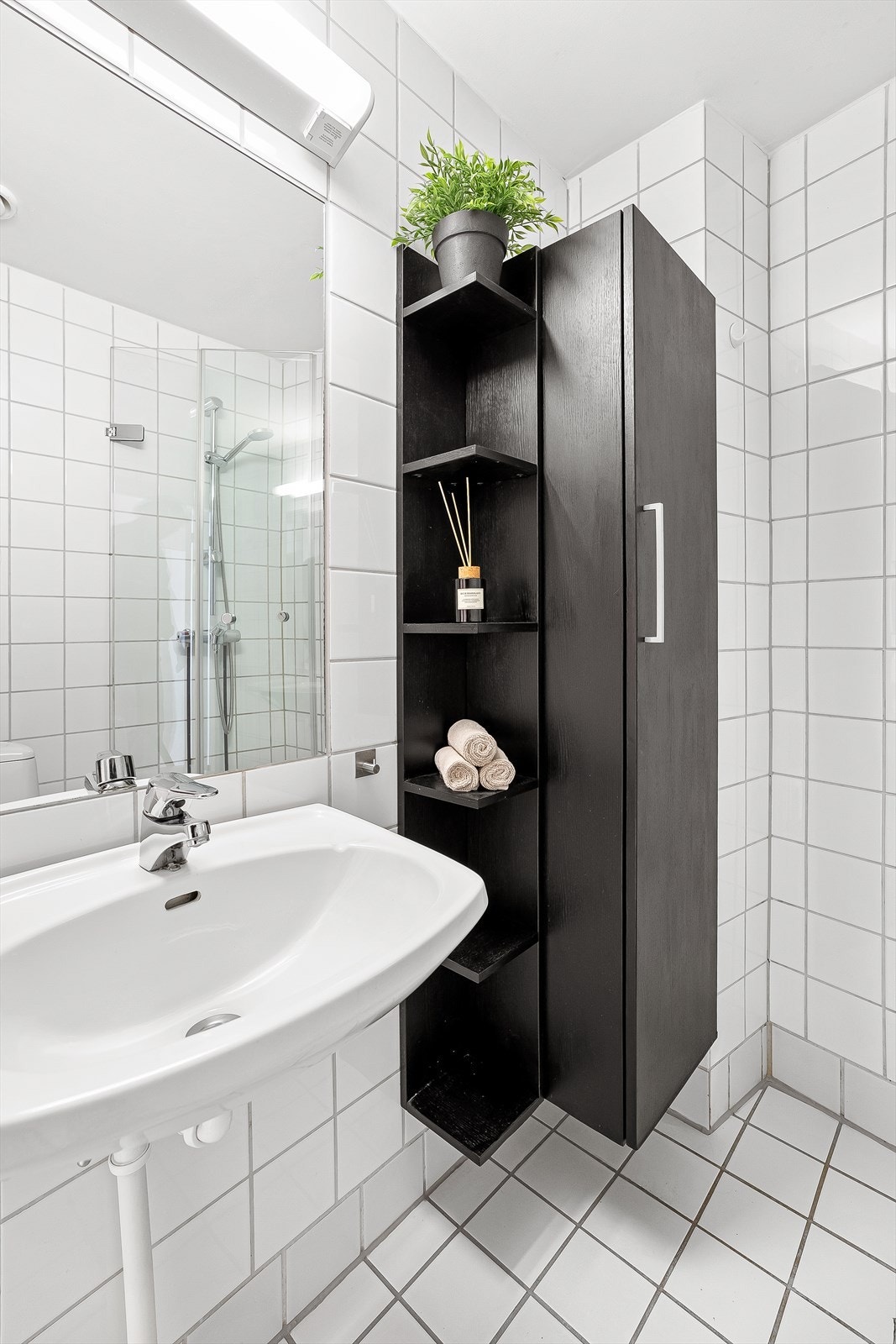 Baderom fra ukjent årstall med opplegg for vaskemaskin, flislagt gulv med gulvvarme, flislagte vegger og malte himlingsflater. Badet er utstyrt med vegghengt servant med ett-greps armatur, speil med overlys og gulvstående toalett. Galleribilde