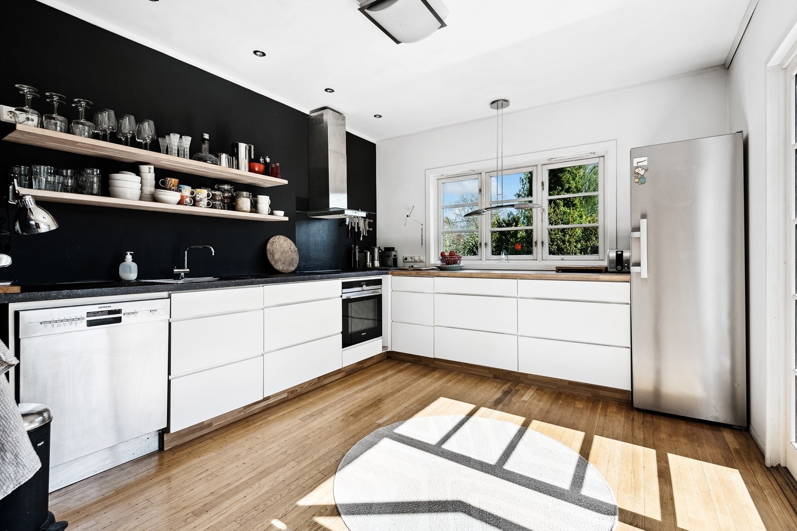 Kjøkkeninnredning bestående av lyse fronter og benkeplate i betong og tre, med integrert koketopp/ovn. Opplegg for oppvaskmaskin og frittstående kjøleskap. Galleribilde