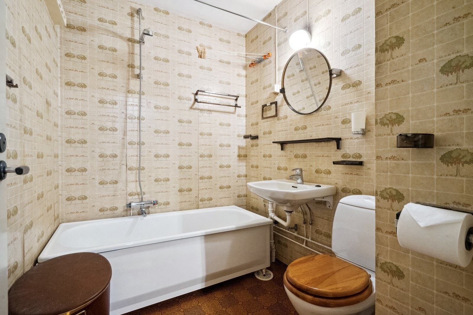 Bad med konstruksjoner fra byggeår, innredet med klosett, servant, stråleovn, badekar med dusj, og innredning i form av en plasthylle og speil. Galleribilde