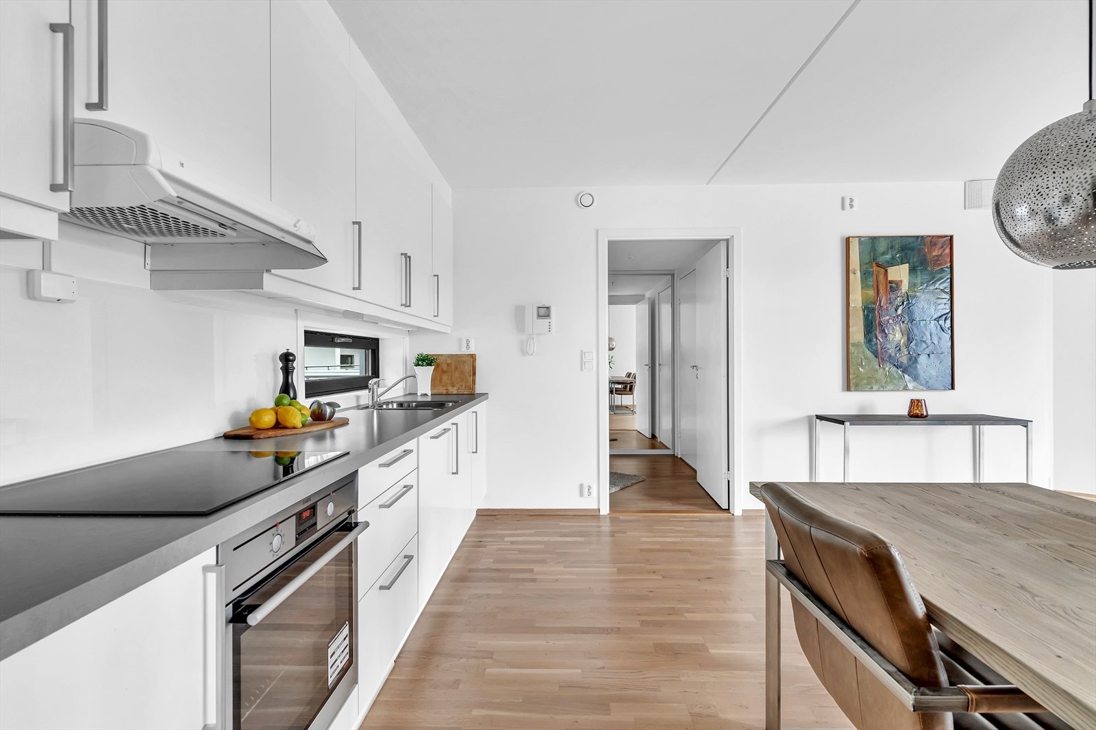 Åpen kjøkkenløsning langs en vegg. Her er det tidløst design med glatte fronter og integrerte hvitevarer. Galleribilde